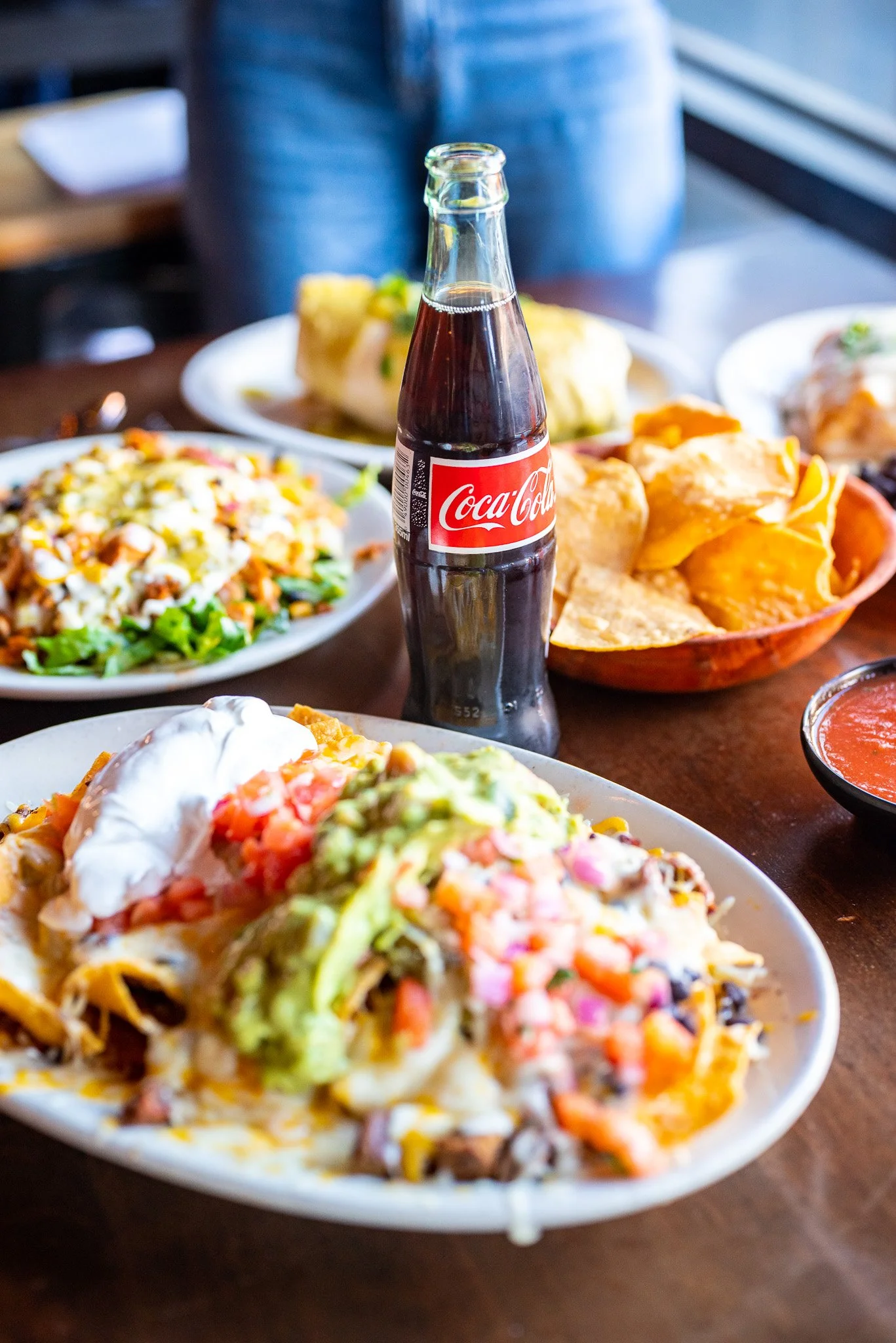 Mexican food, such as nachos & a burrito, tortilla chips and a cola on a table at Howling Wolf Taqueria