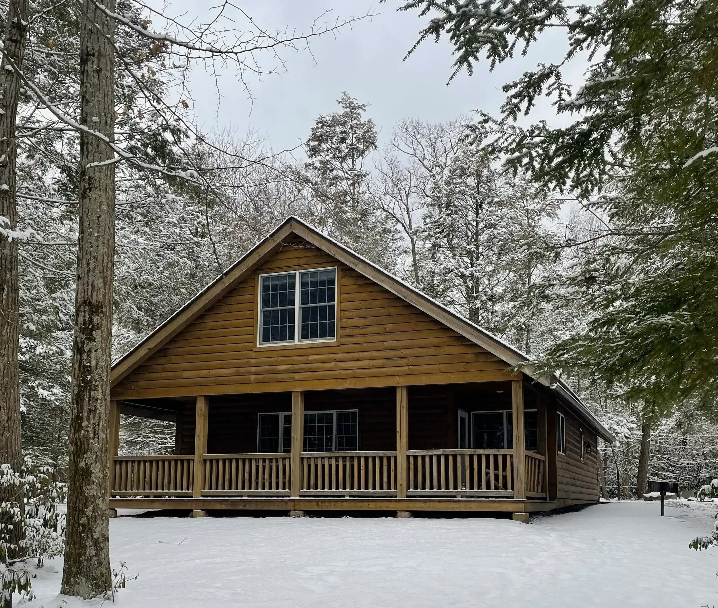 A wooden house with a porch surrounded by snow and trees, during winter.