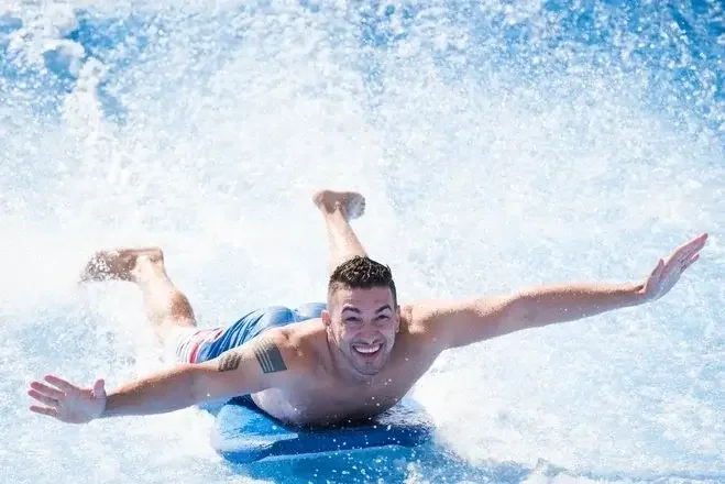 Man in blue shorts sliding on water with a big smile, arms outstretched.