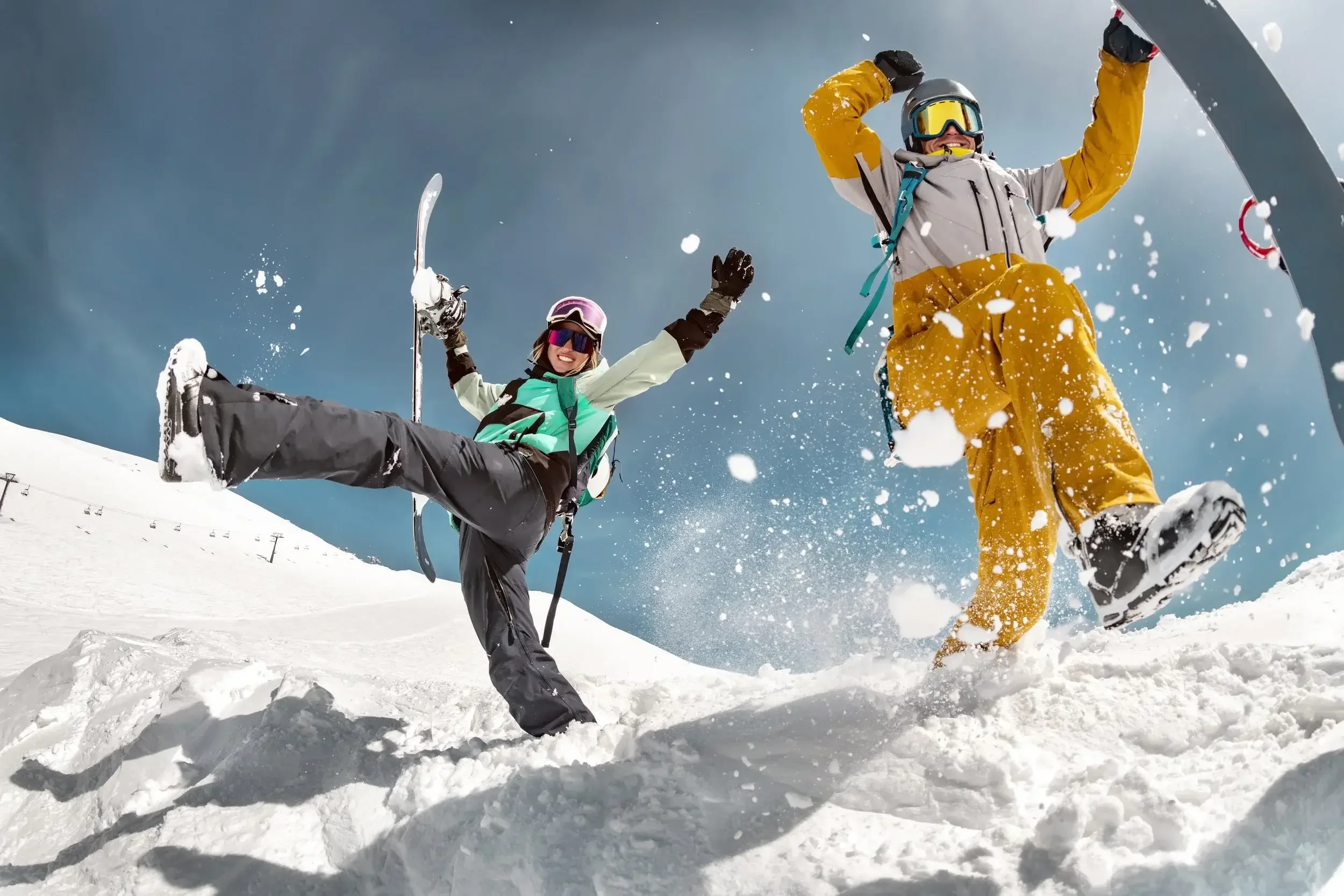 Two people in ski gear celebrating and enjoying snow while skiing on a snowy mountain under a clear sky.