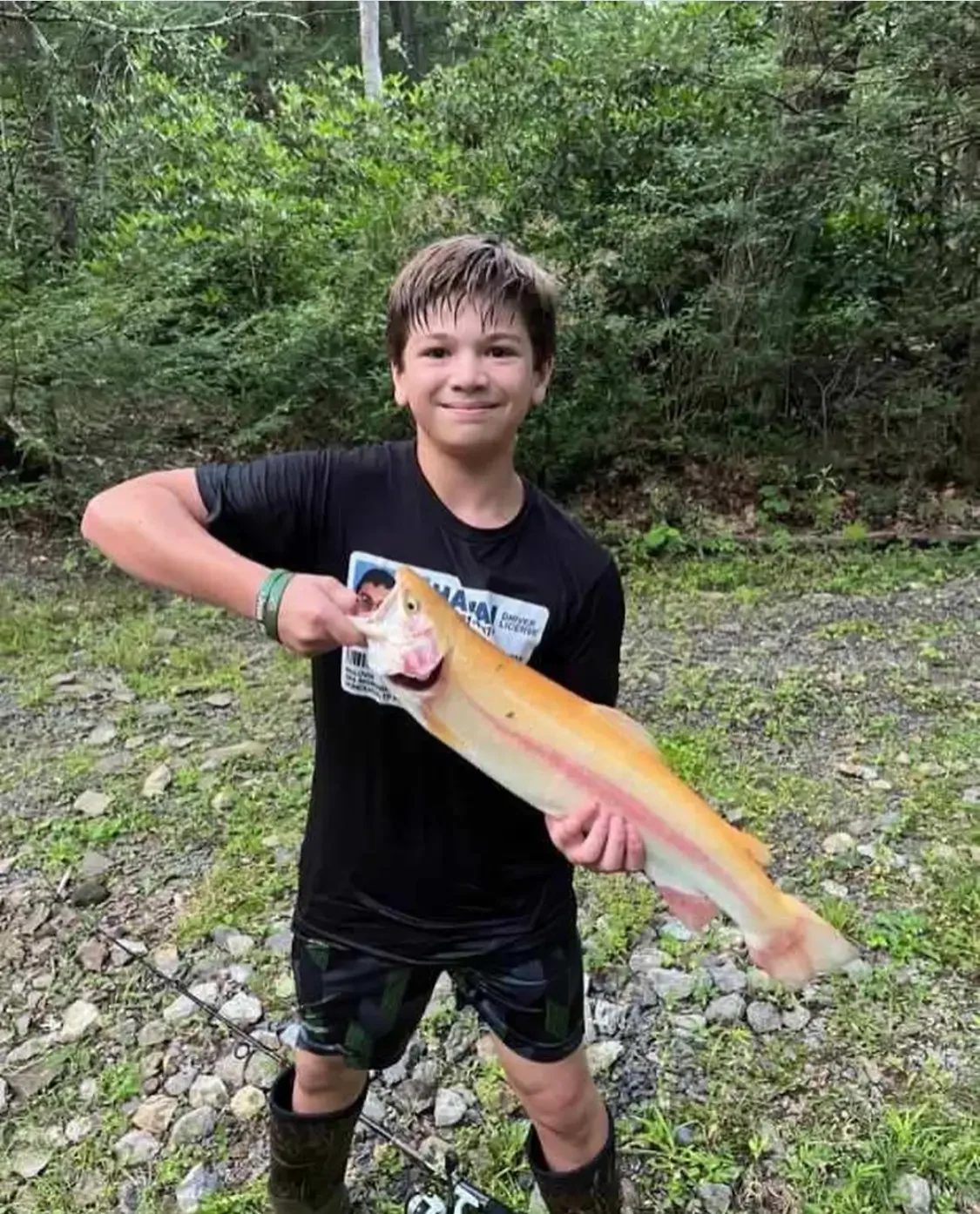 Boy holding a large golden rainbow trout after fishing.