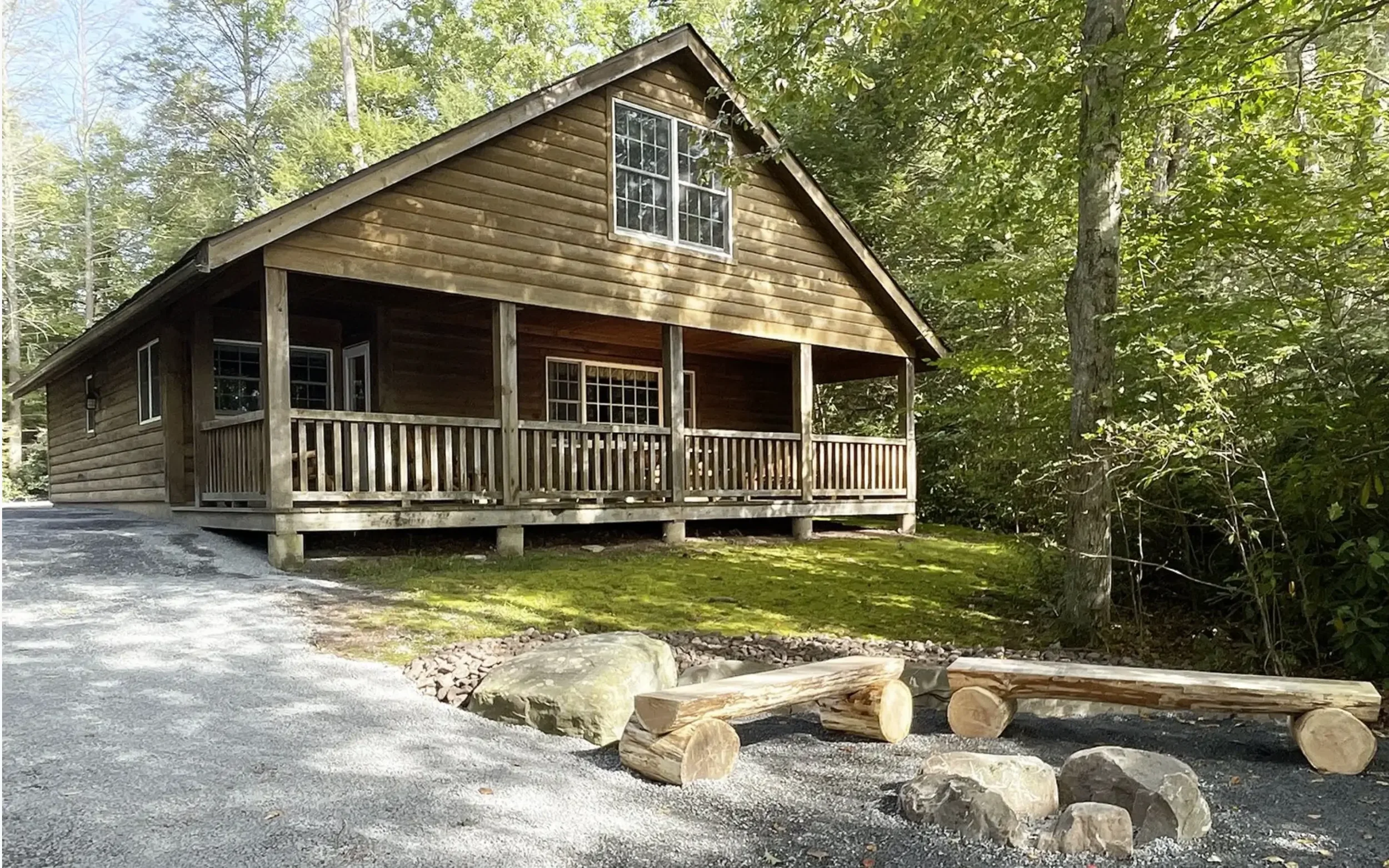 A wooden cabin with a front porch surrounded by trees and lush greenery.