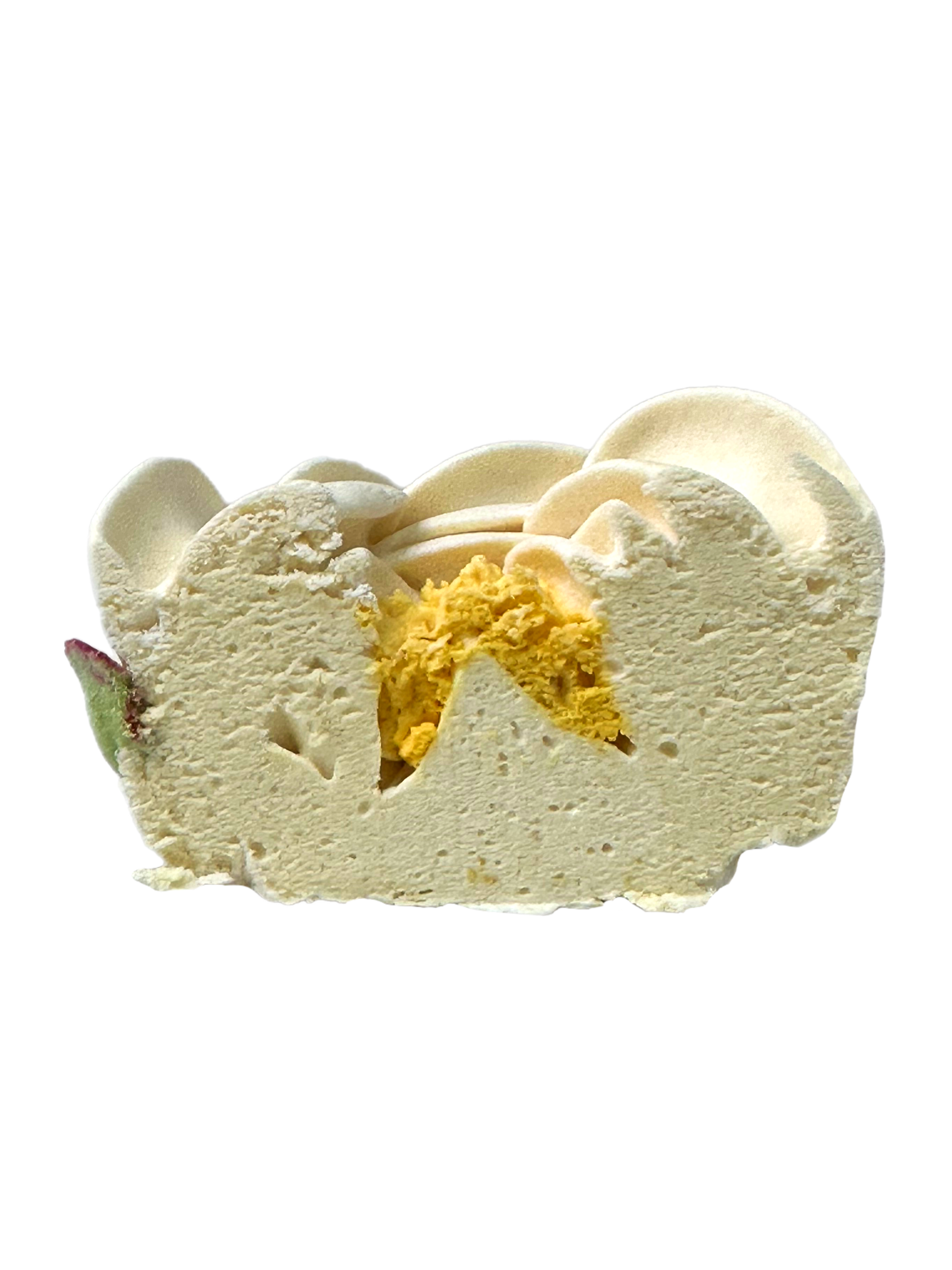 Slice of white ice cream with a yellow filling and a decorative swirl on top, with a small piece of fruit on the side.