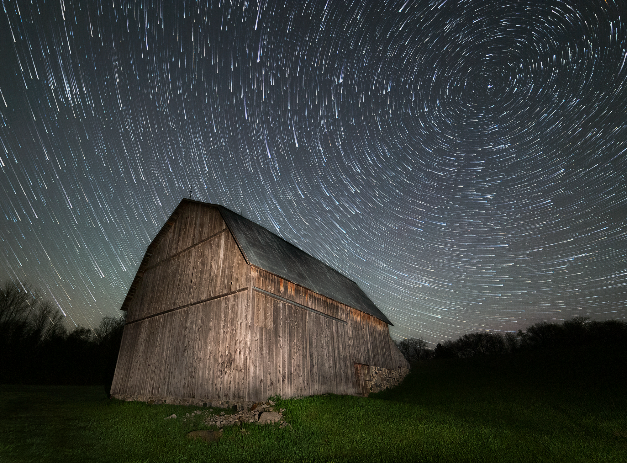 Finished star trail photograph of a light-painted barn under circular star trails at night