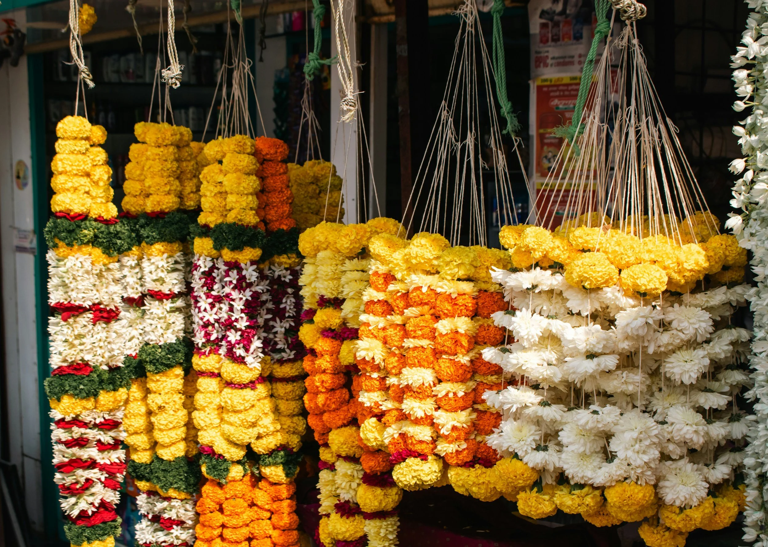 Hanging flower garlands made of marigolds and other flowers at a market stall.