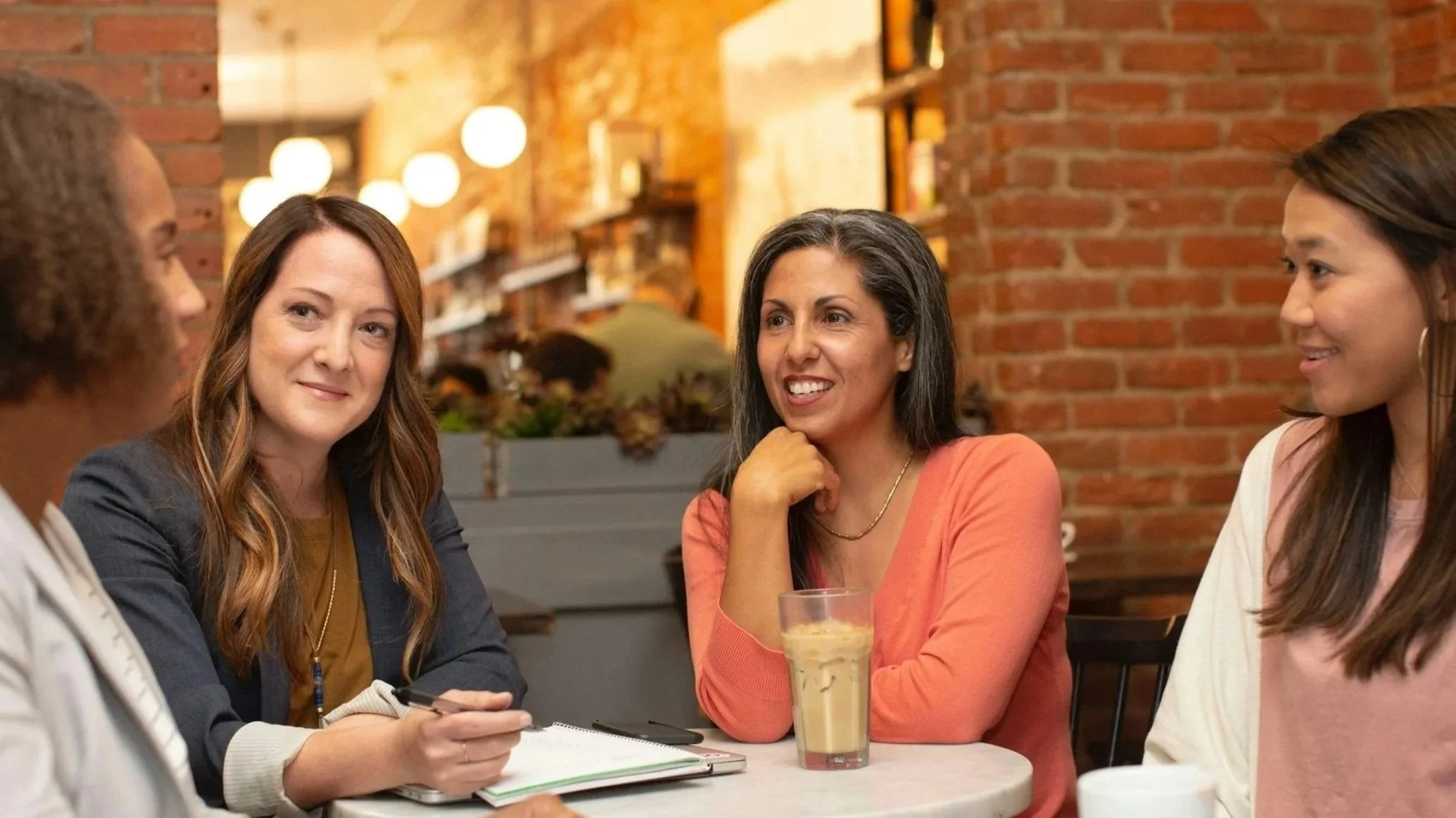 Group of four women having a meeting at a cafe, sitting around a table with coffee and a tablet.