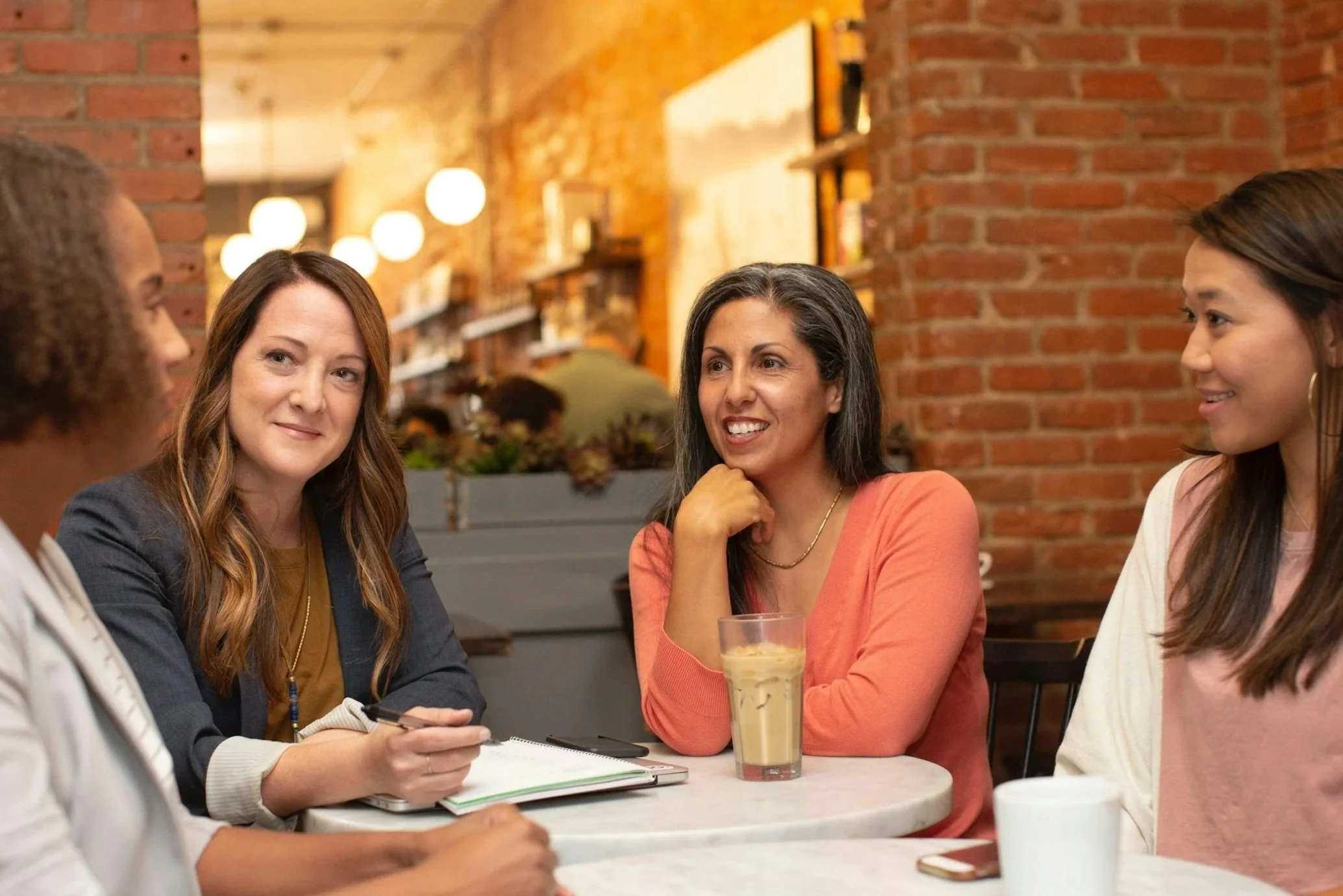 Group of four women having a meeting at a cafe, sitting around a table with coffee and a tablet.