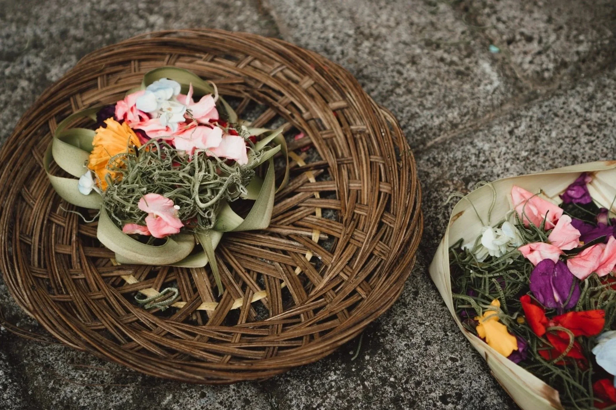 Colorful flower arrangements with various petals, some wrapped in green ribbon and some inside a basket on a textured surface.