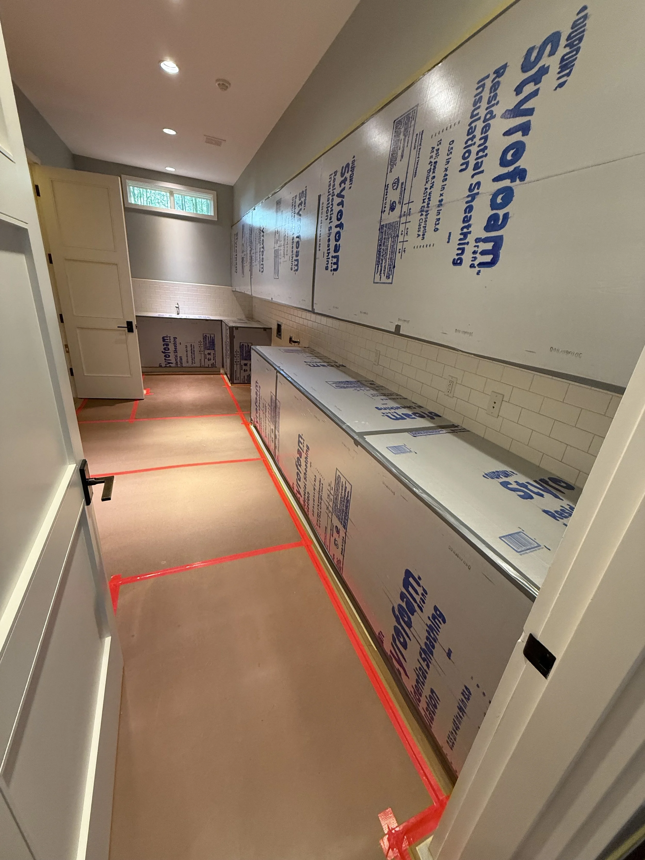 A kitchen under construction with drywall covered in blue and white insulation sheets labeled 'Styrofoam' and red painter's tape marking the floor boundaries.