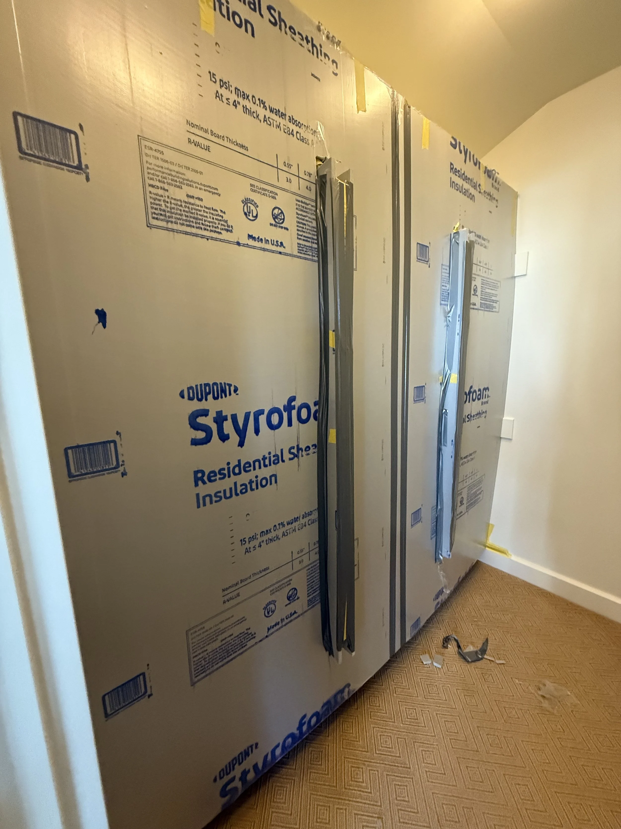 A wall with insulation panels and mounting brackets, with some tools and debris on the floor nearby.