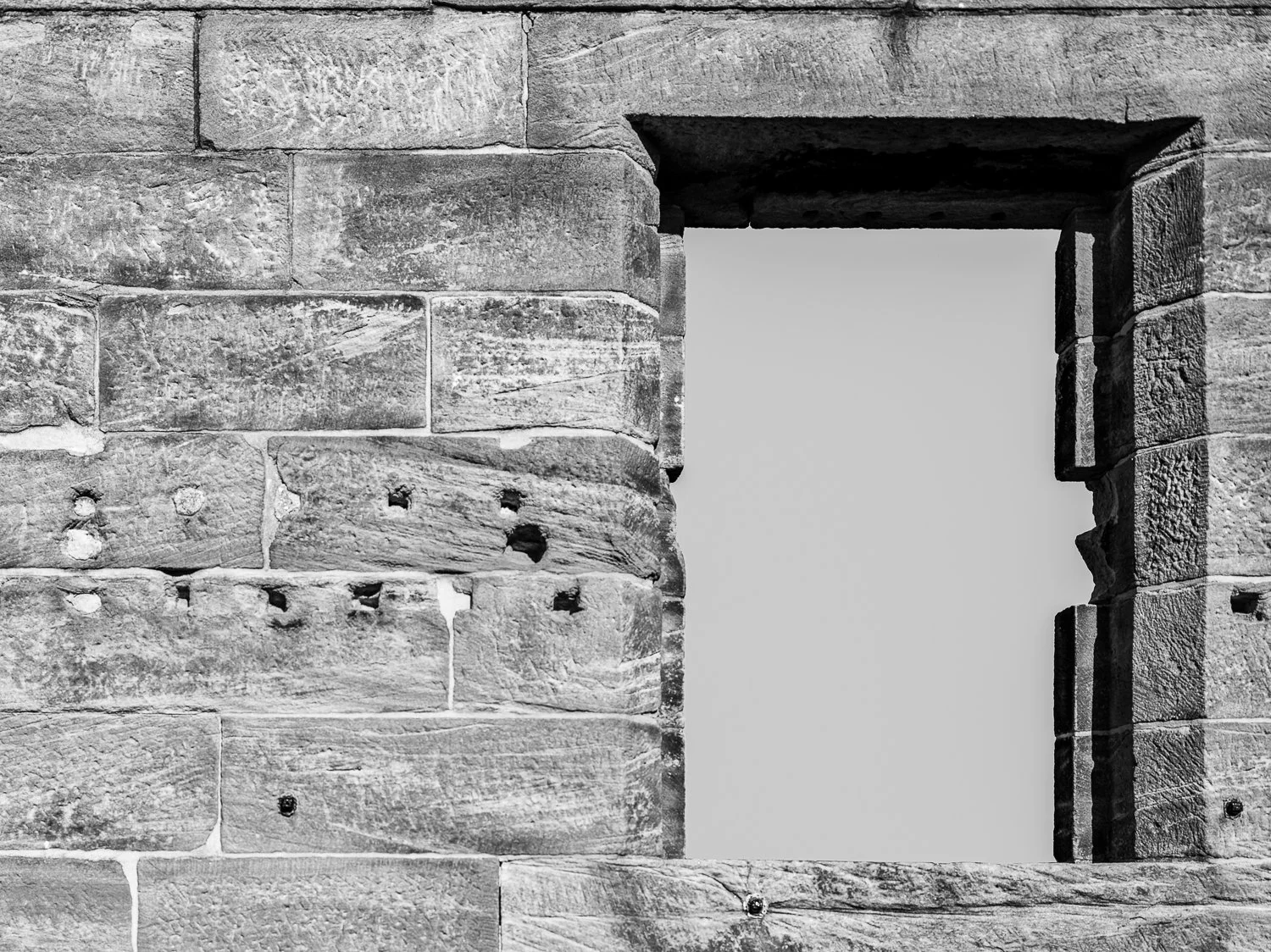A black and white photo of an old stone wall with a rectangular opening, revealing an empty sky.