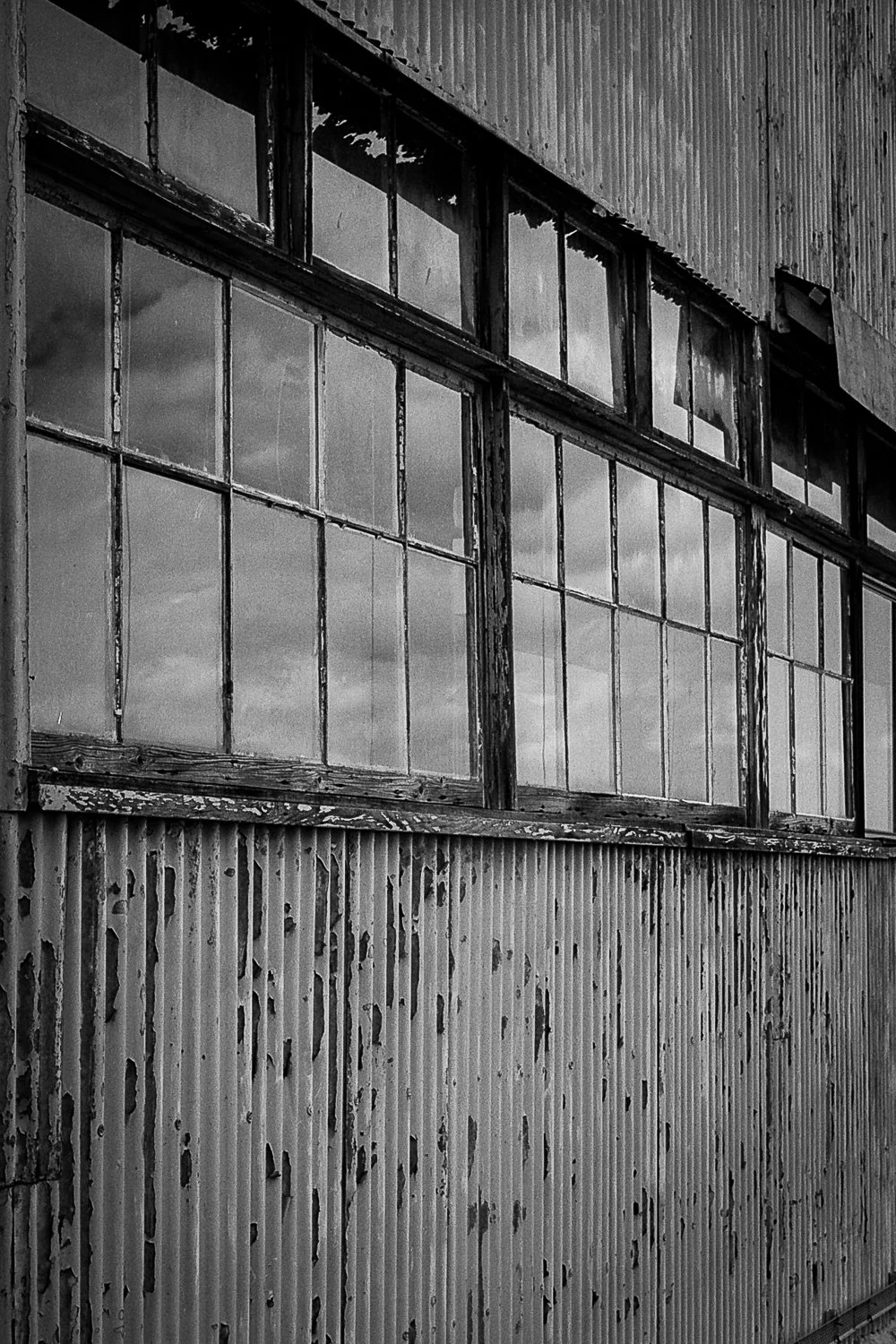 Black and white photo of an old, weathered building with large, multi-pane windows and a corrugated metal exterior.