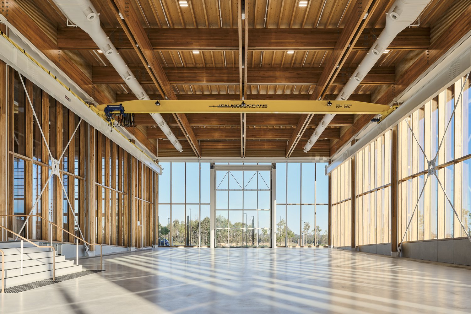 Large modern industrial interior with wooden ceiling, expansive windows, and a yellow overhead crane.