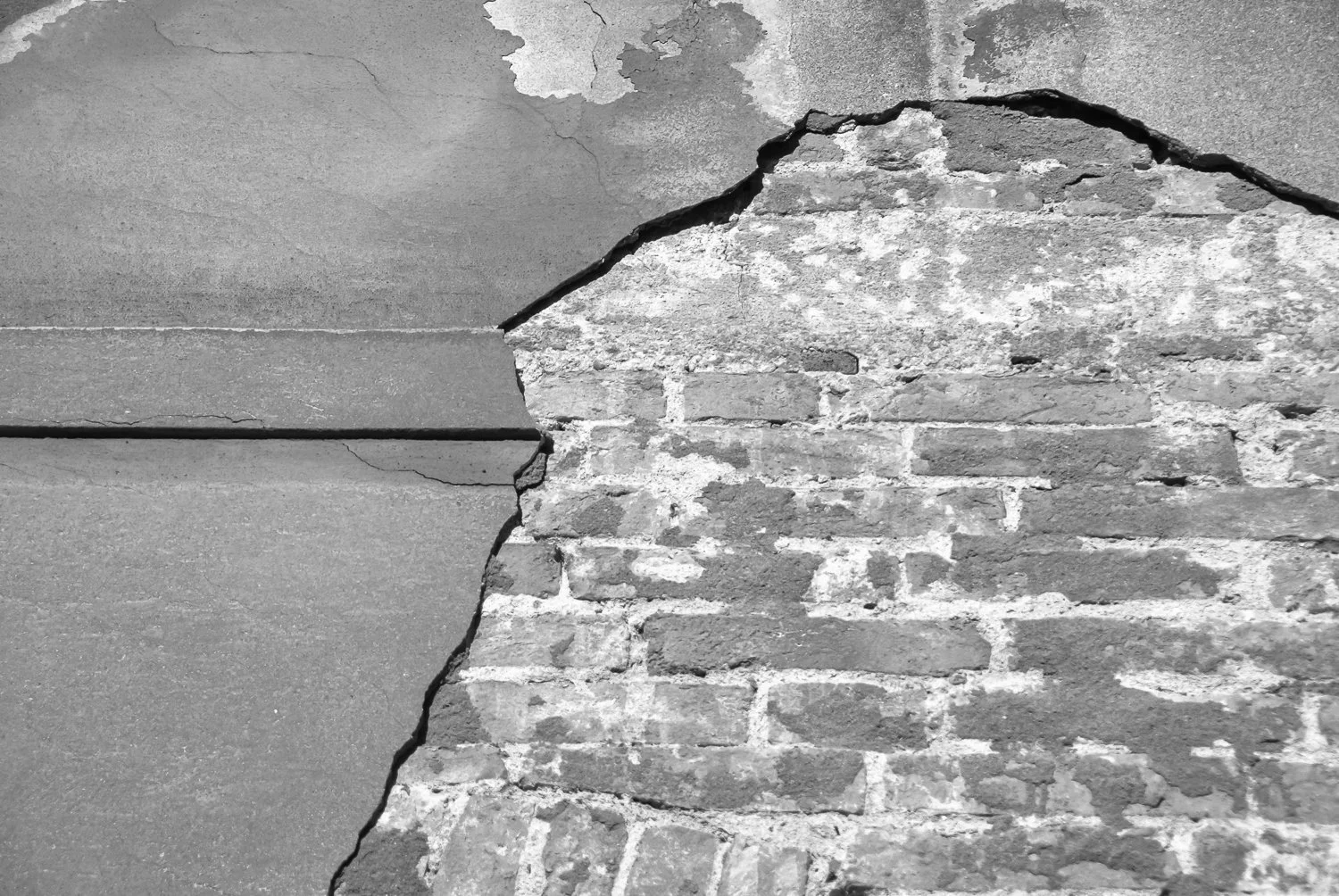 A close-up of a wall with peeling paint and exposed brick, showing cracks and deterioration.