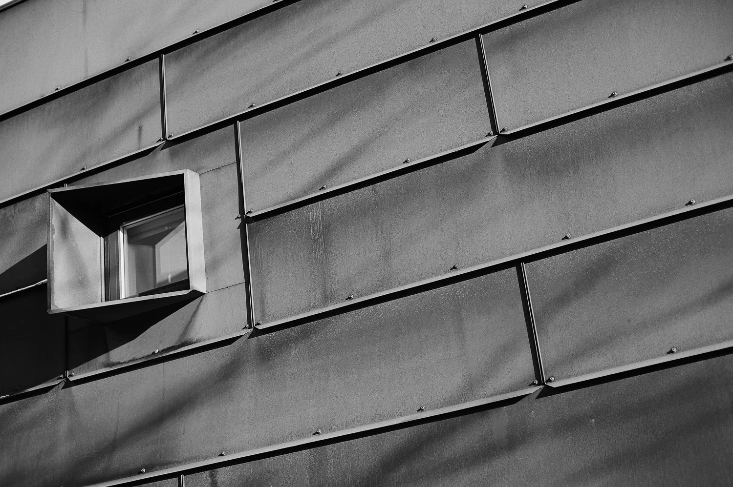 Close-up of a modern building's metal exterior with a small protruding window box, black and white photograph.