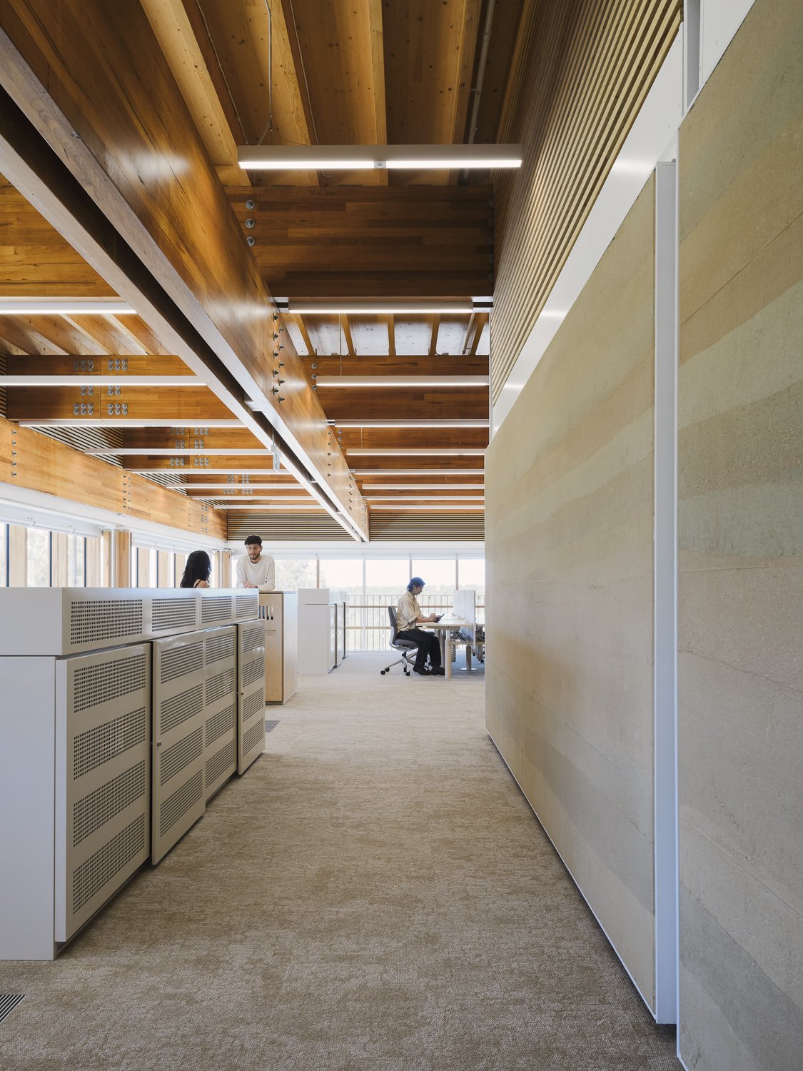 Modern office interior with wooden ceilings, carpeted floors, and people working at desks.