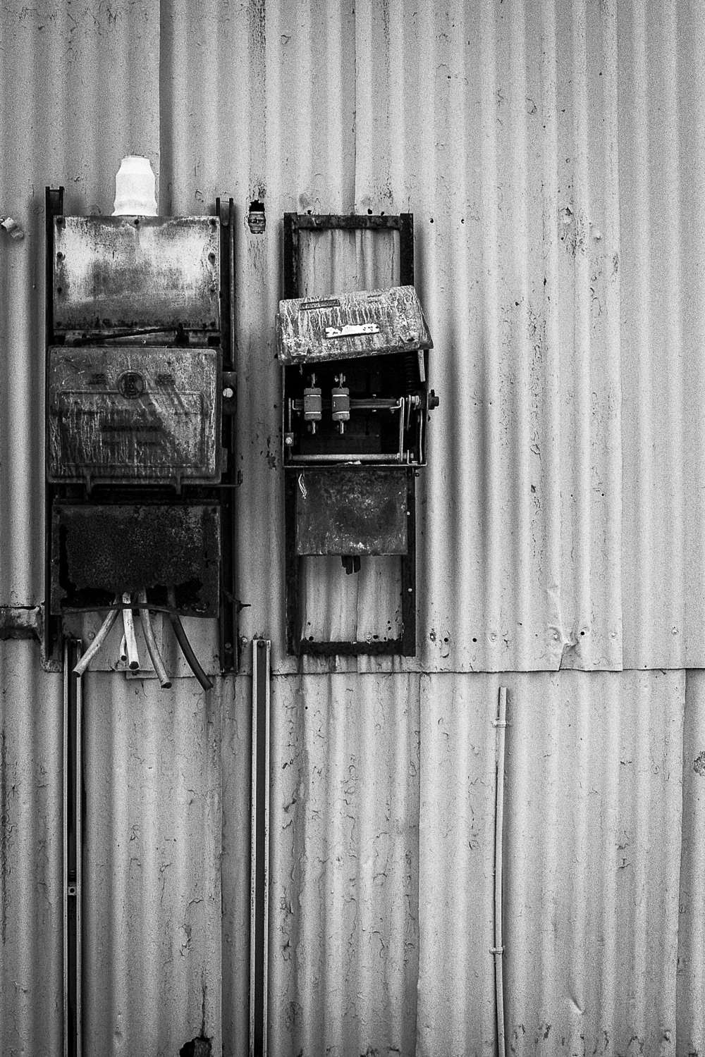 Old, rusty electrical panels mounted on a corrugated metal wall.