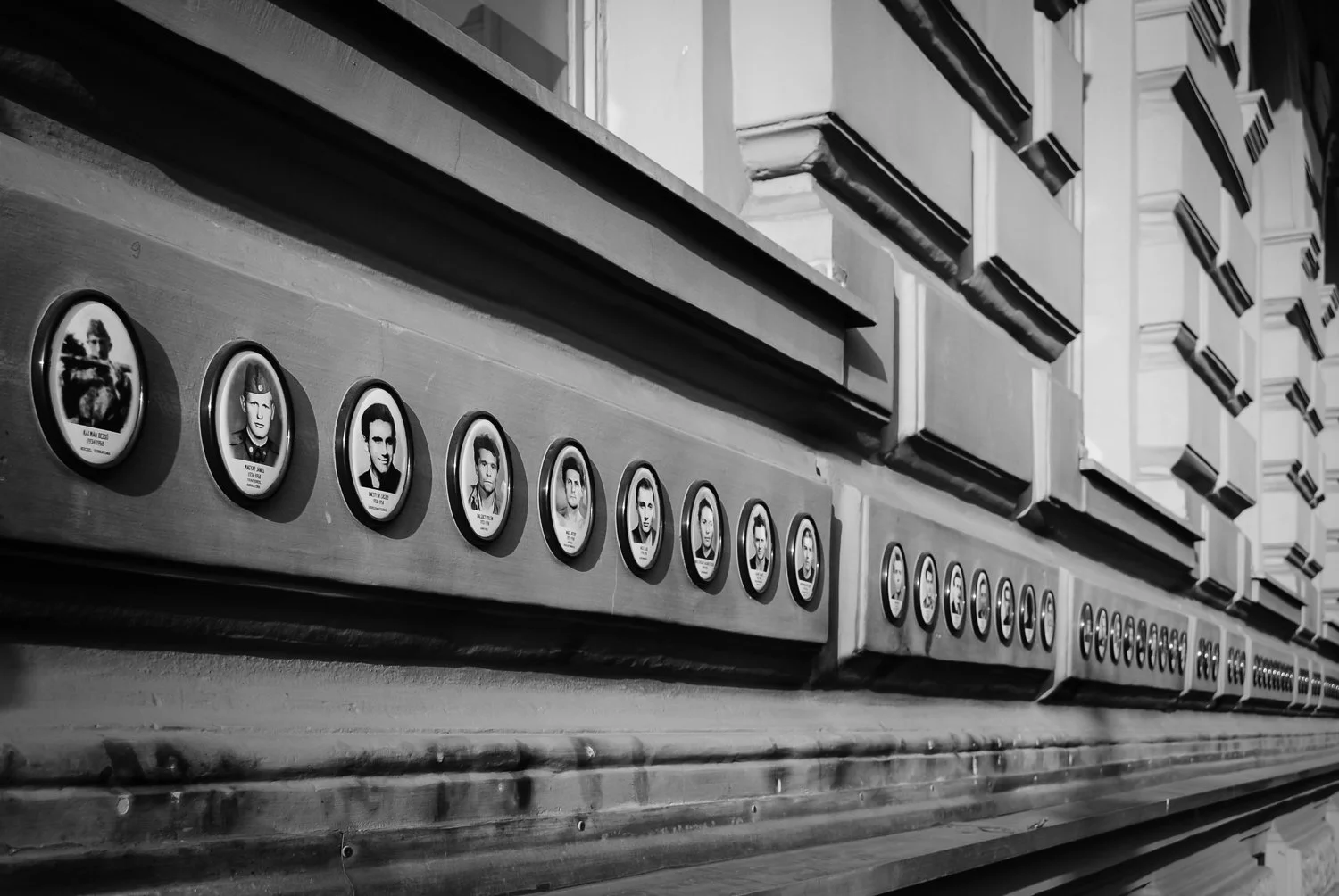 Black and white photo of a wall with framed portraits of individuals on a wooden ledge.