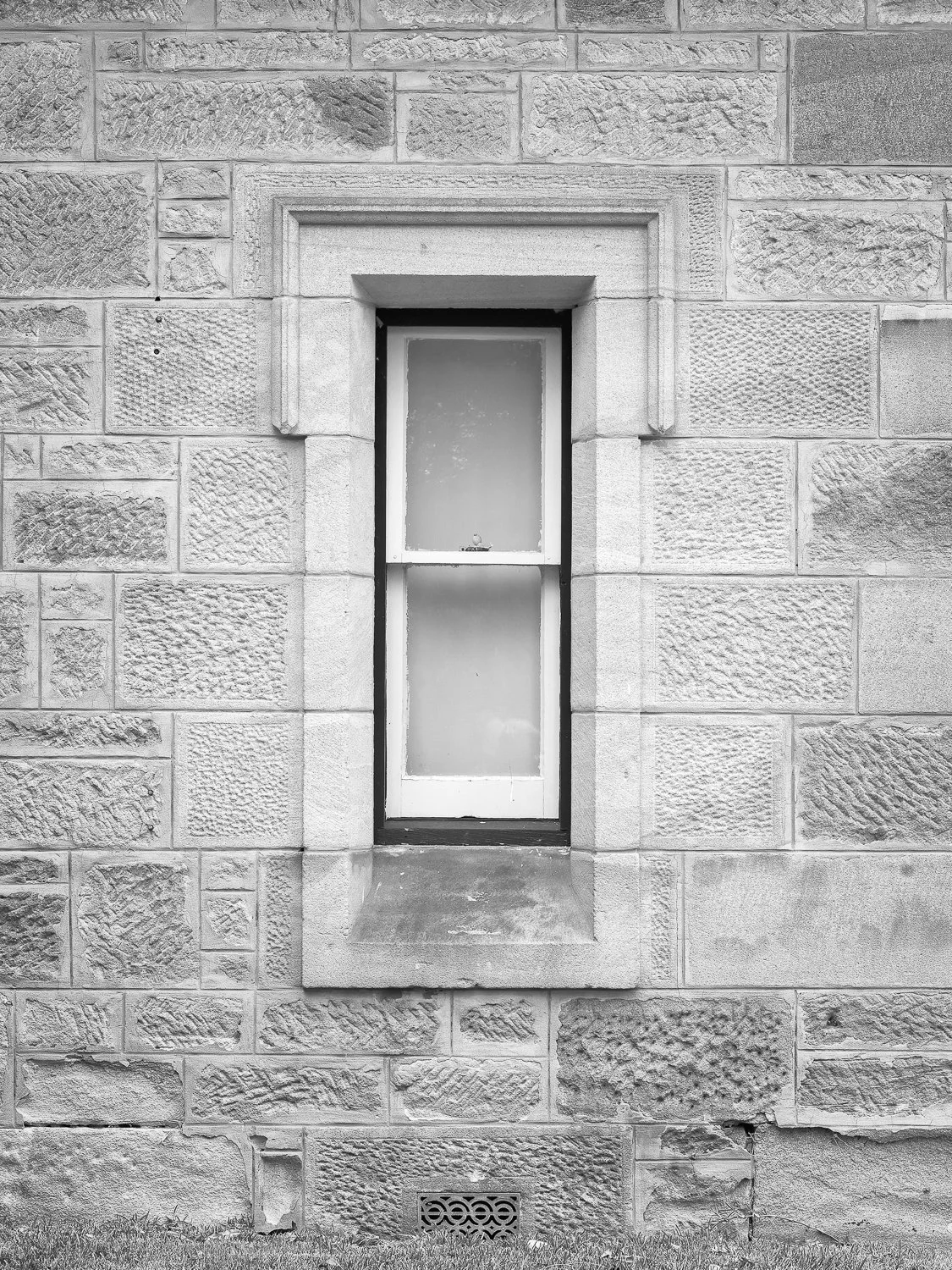A small narrow window set in a stone wall building, with a stone ledge below it and a decorative stone border around the window.