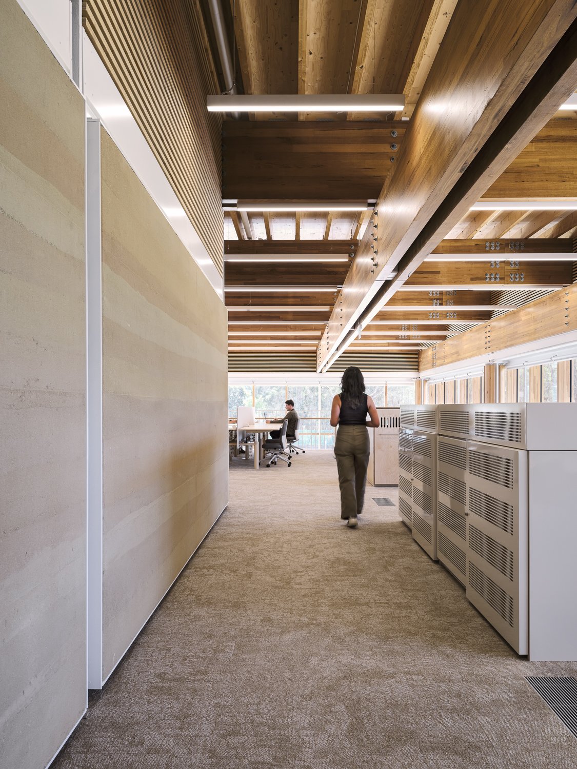 Office hallway with modern wooden ceiling, open workspace, and person walking.