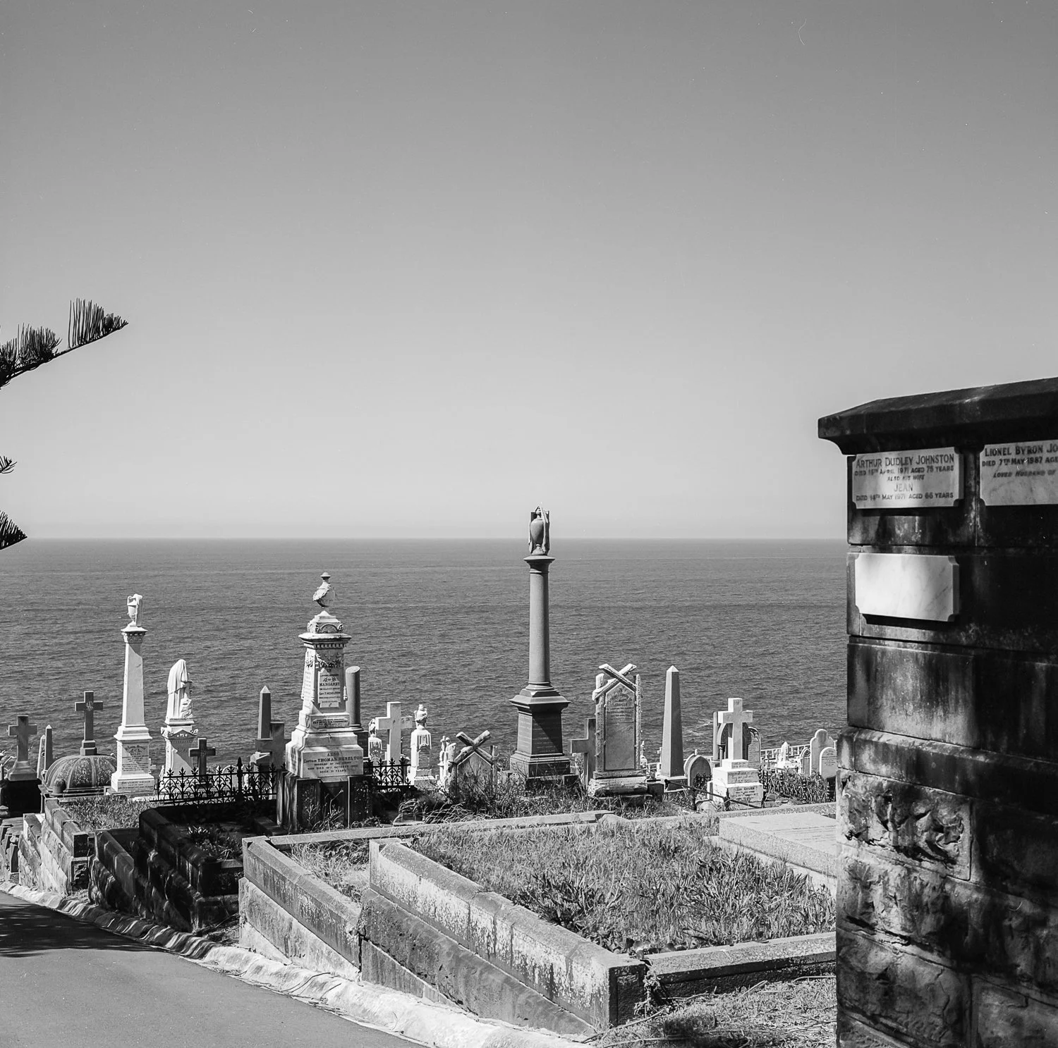 Black and white photo of a cemetery with tombstones and crosses overlooking the ocean, with a clear sky in the background.