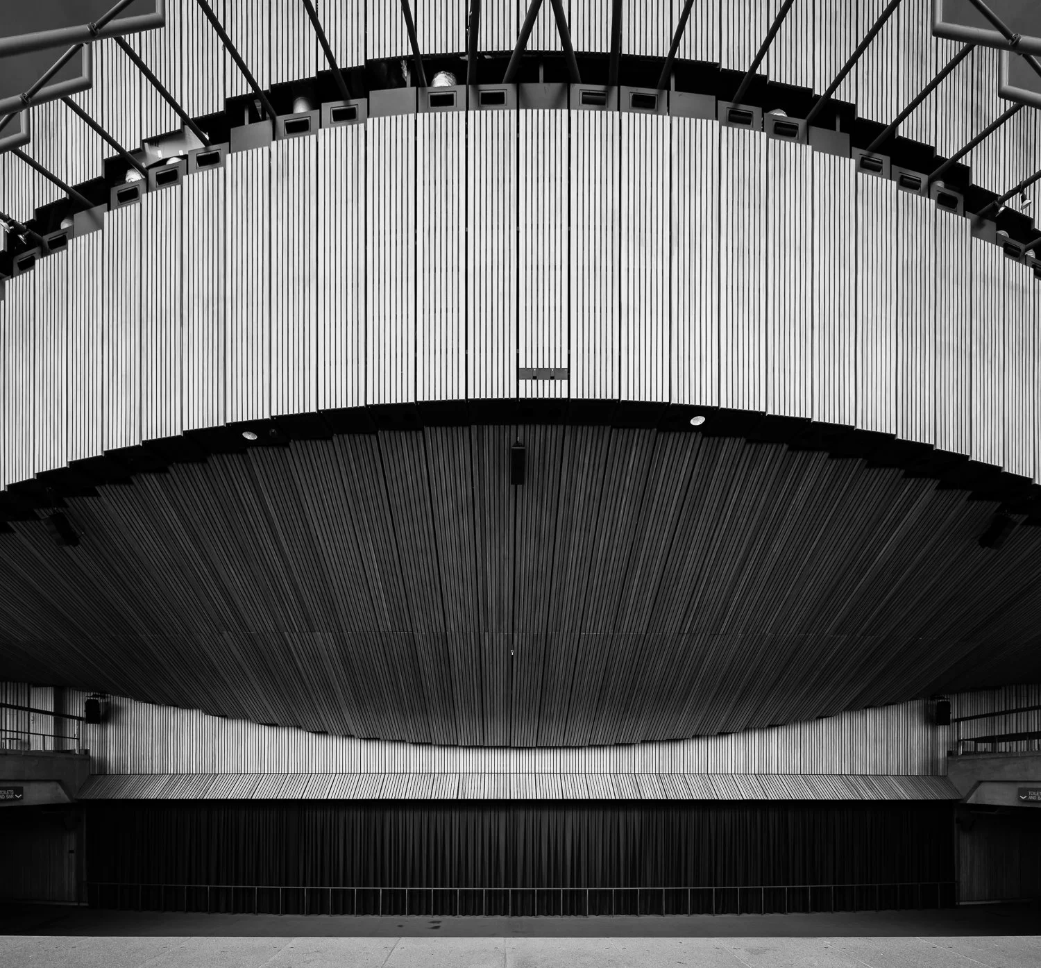 Black and white interior of a modern theater or concert hall with architectural design featuring circular layered ceiling and walls with vertical panels.
