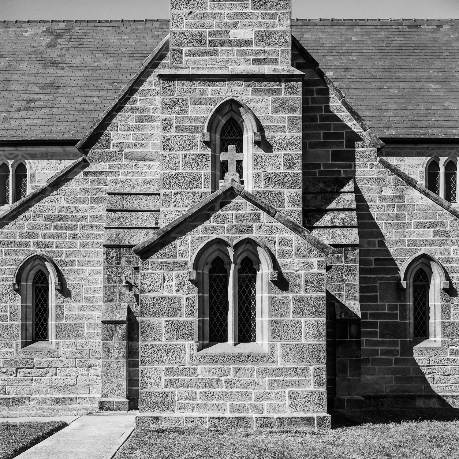 Black and white photo of a stone church with arched windows, a crossing, and a cross in the center.