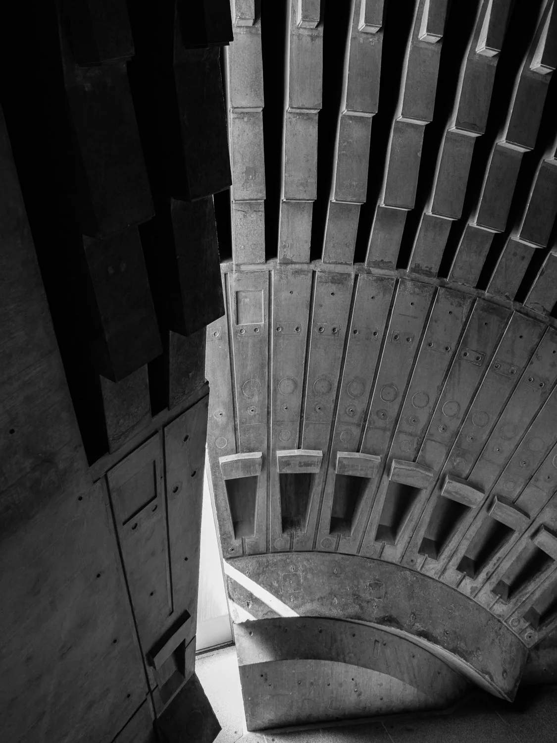 Black and white photo of a curved concrete staircase viewed from above, with rectangular steps and a small opening at the top.