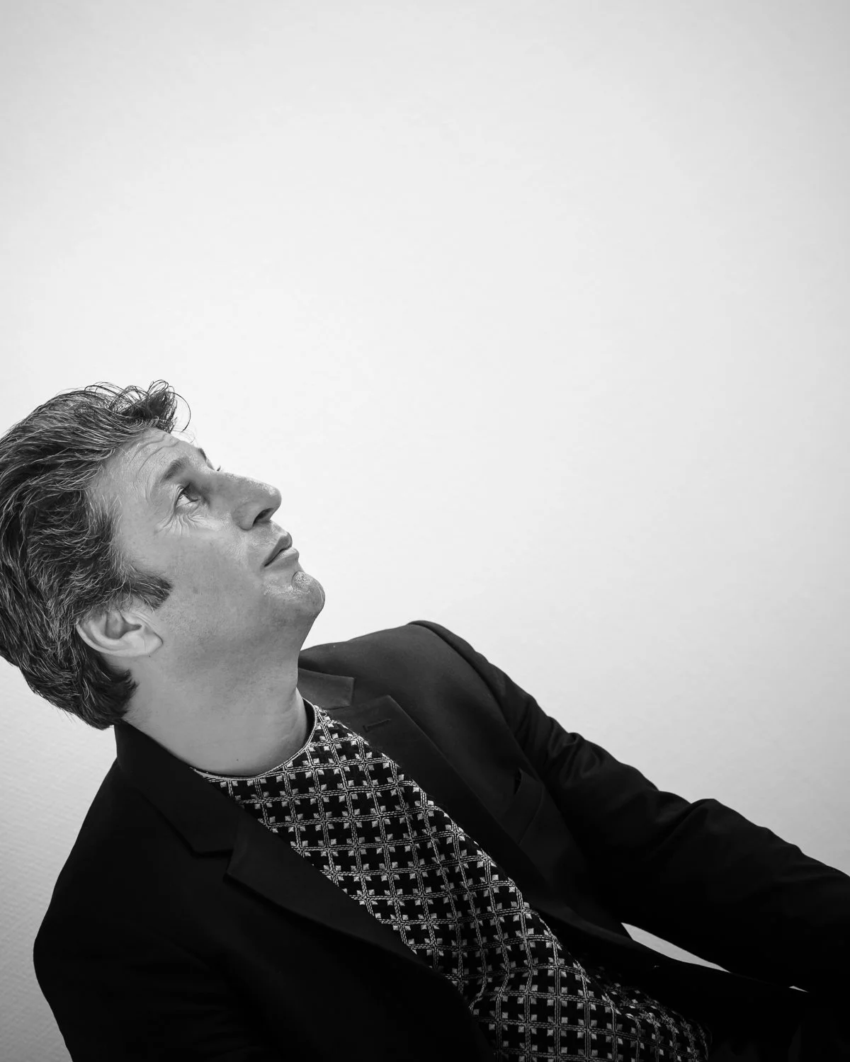Black and white portrait of a man looking upwards with a surprised or contemplative expression, wearing a suit and patterned shirt.