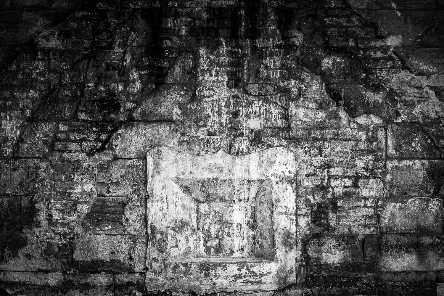 Black and white photo of a weathered brick wall with a worn, painted sign bearing an arrow pointing left.