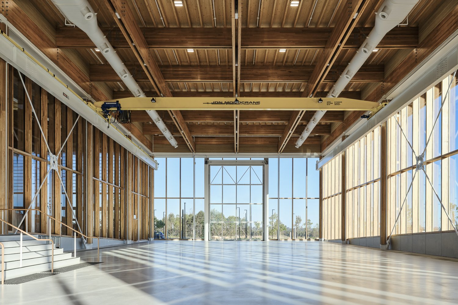 Empty indoor space with large glass windows, wooden ceiling, and an overhead crane, under construction or renovation.