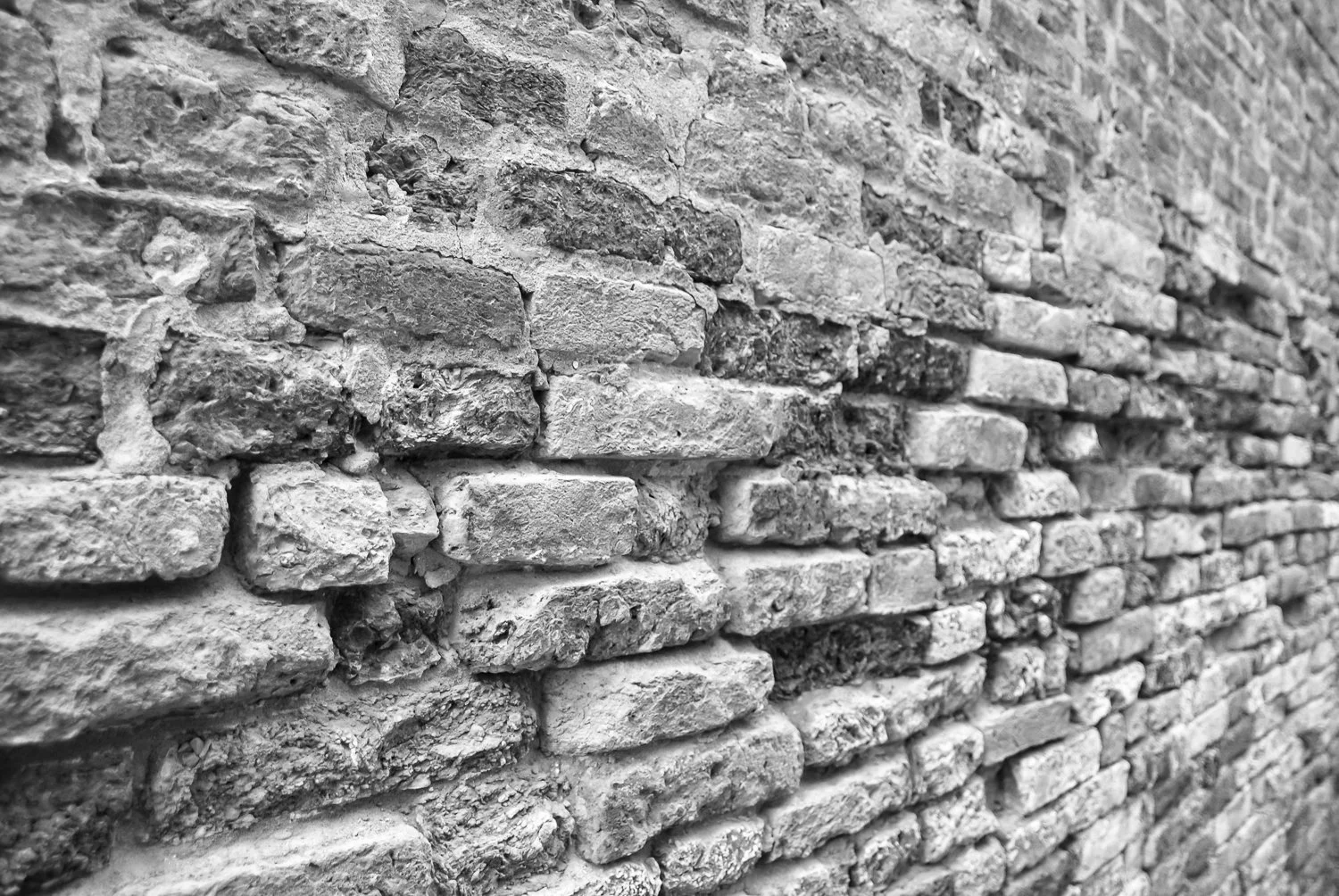 Black and white photo of a rough brick wall with uneven bricks and mortar.
