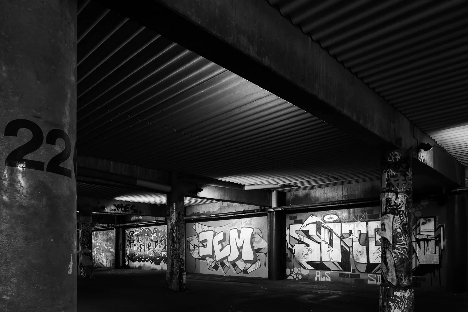 Black and white photo of an urban underpass with graffiti-covered walls and concrete pillars.