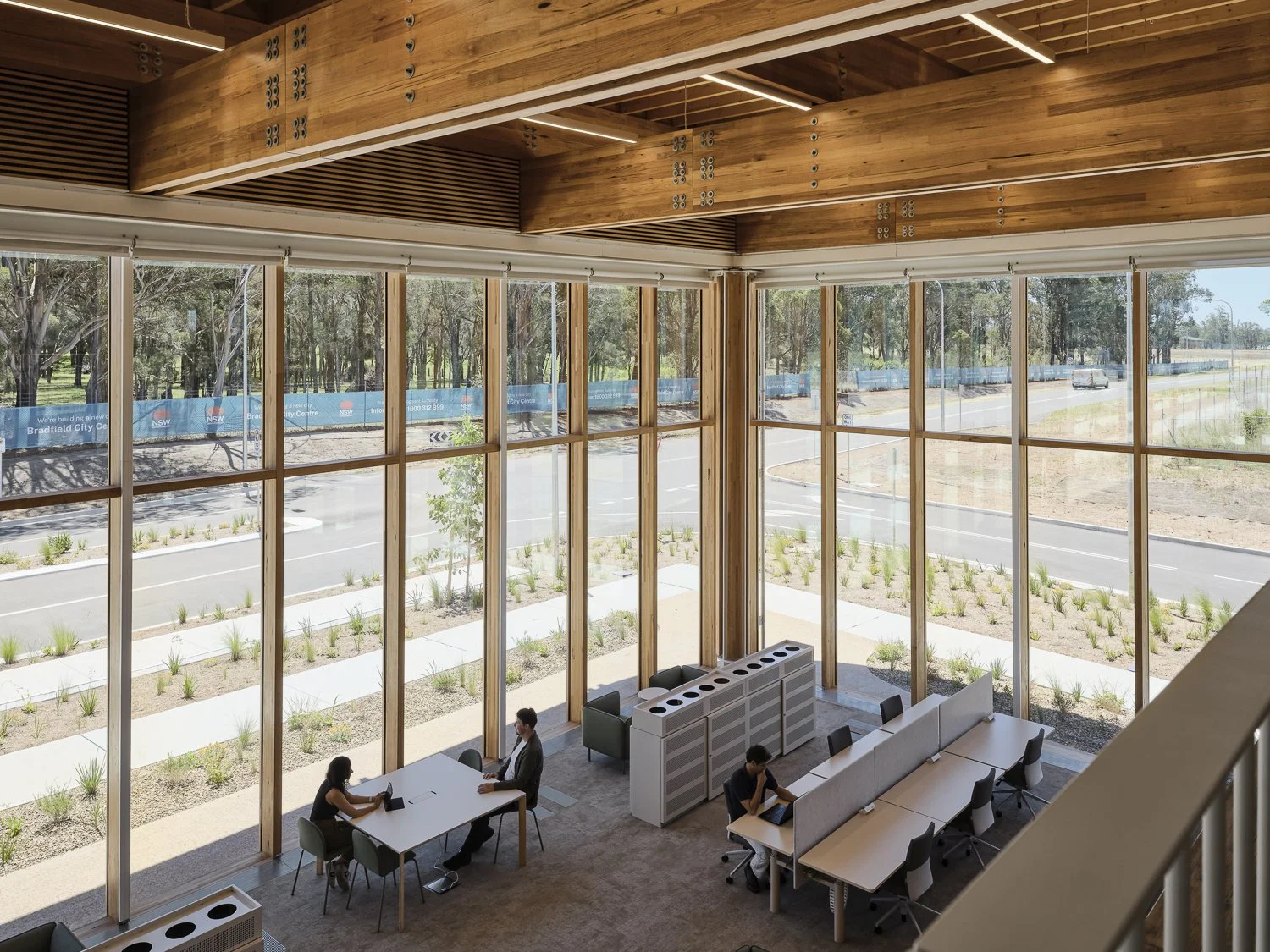 Interior of a modern office space with large floor-to-ceiling windows, a mix of individual and group work areas, and minimalistic furniture during daytime.