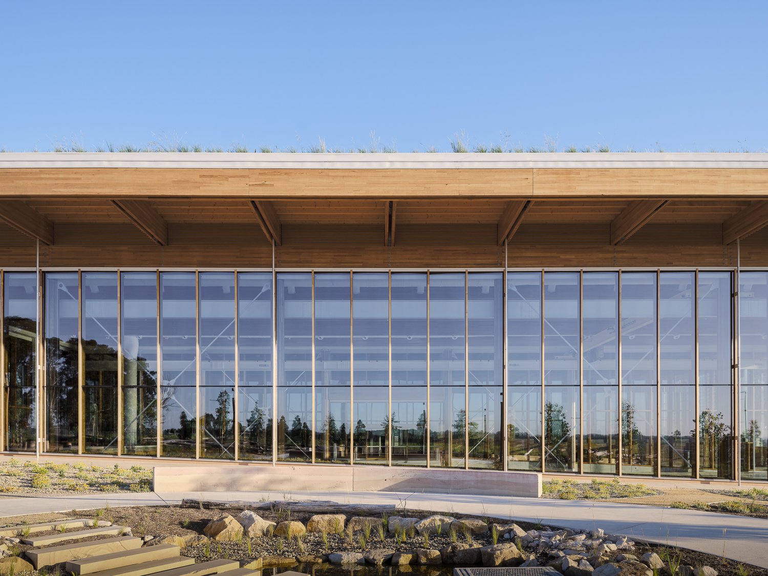 Modern building with large glass windows and wooden beams under a clear blue sky.