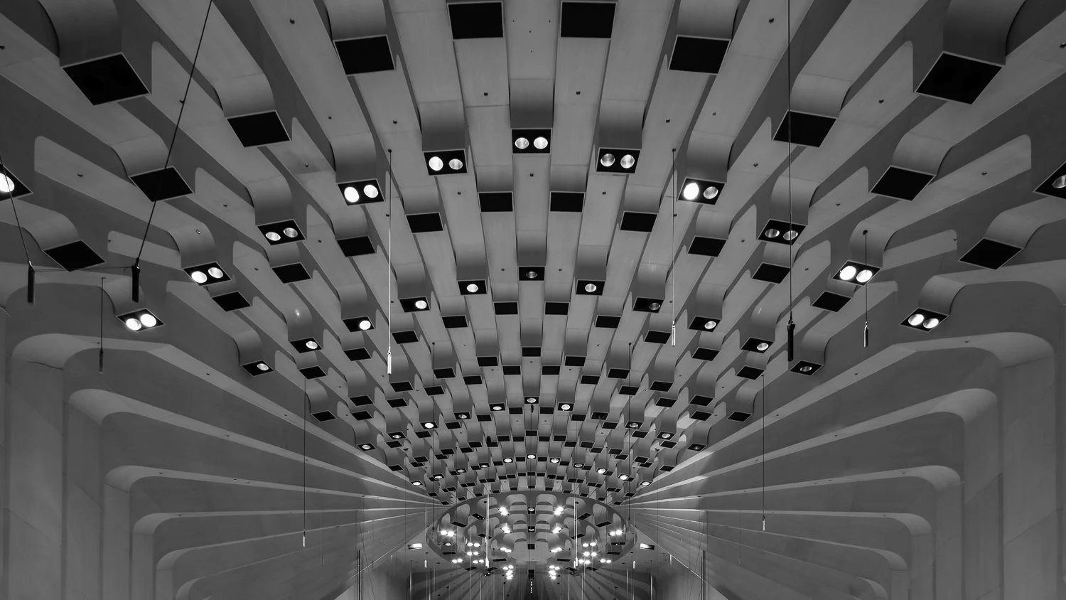 A black and white photograph of a modern, geometric ceiling with multiple hanging lights.