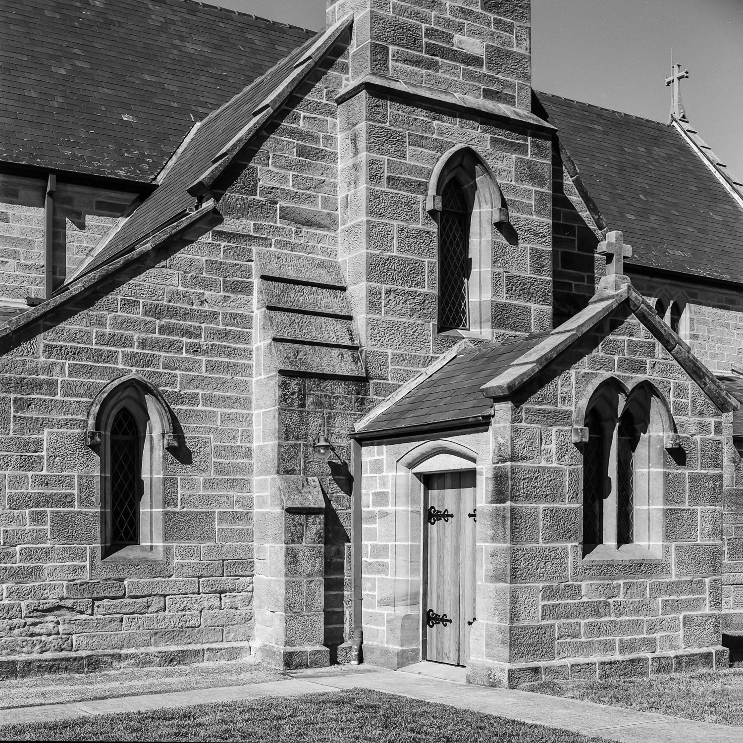 A black and white photo of a stone church with arched windows and a wooden door, featuring Gothic architectural details.