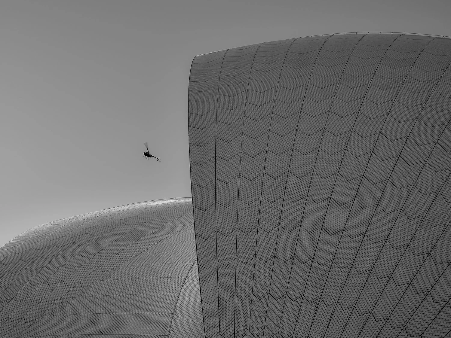 A helicopter flying above modern architectural buildings with smooth curved surfaces.