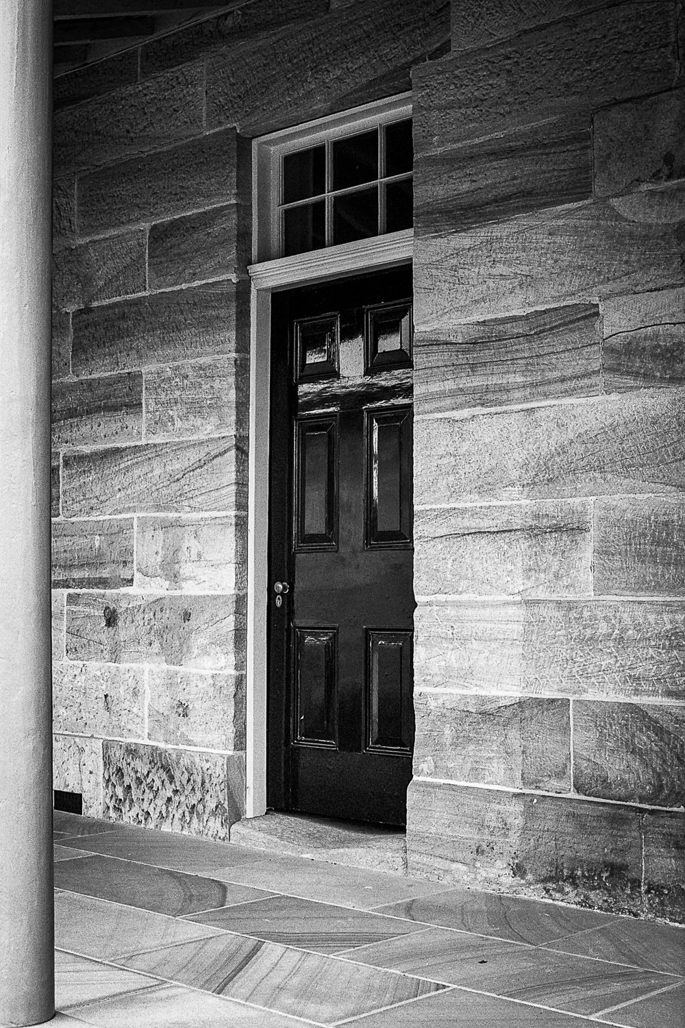 Black door with gabled window above, set in stone wall, with tiled floor in front.