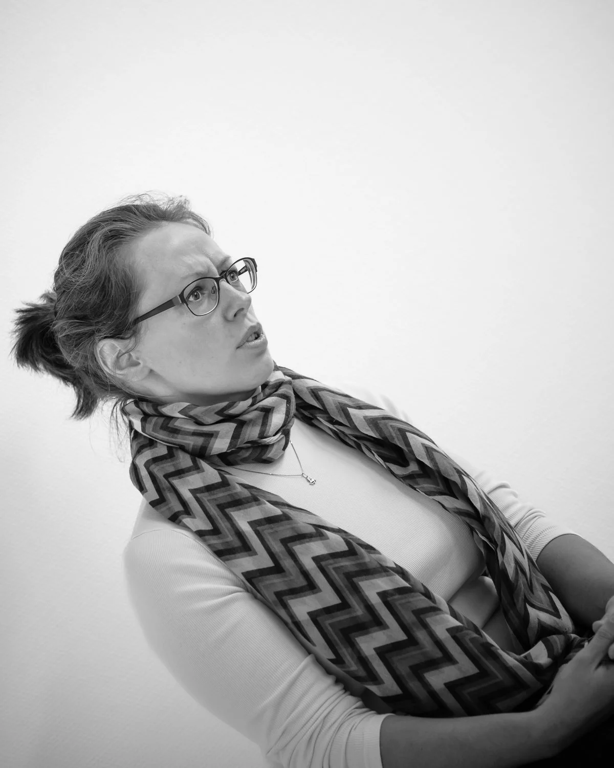A woman with glasses and a patterned scarf is looking to her left with a surprised or confused expression.