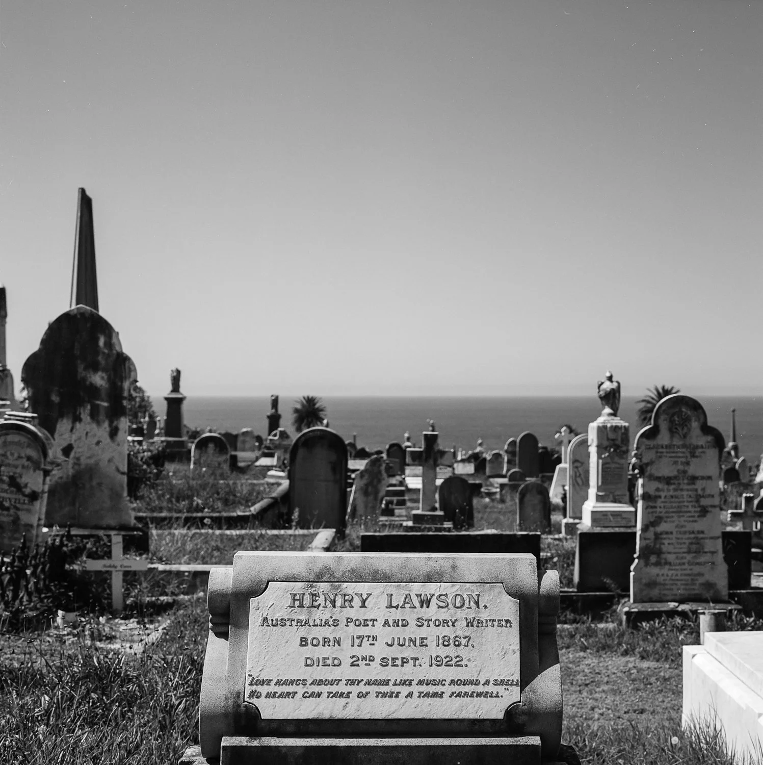 Graveyard with tombstones overlooking the ocean, with several statues and palm trees in the background.