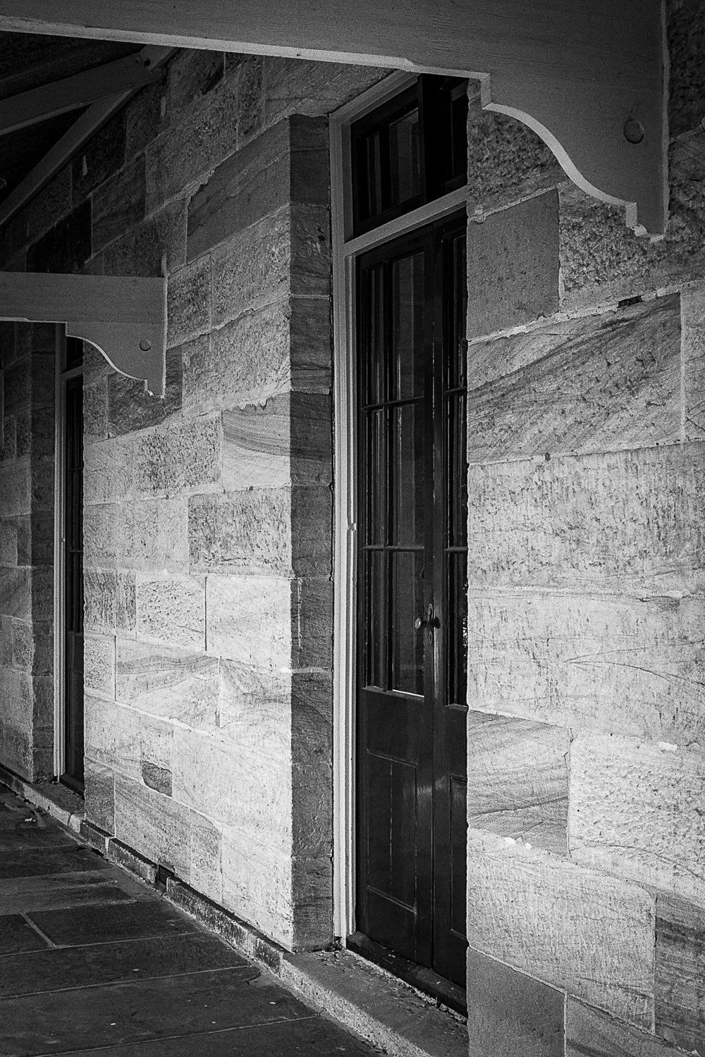 Black and white photo of a stone building with a black door and large storm window.