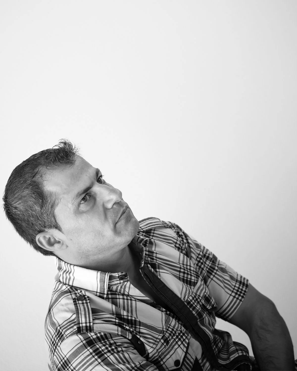 A black and white portrait of a man in a plaid shirt, looking upward and to the left, with a serious expression.