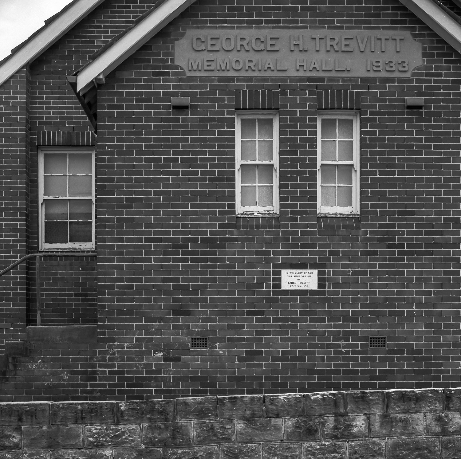 Black and white photo of the brick exterior of Georges H. Trevitt Memorial Hall built in 1933, with three windows, a small plaque, and a stone foundation.