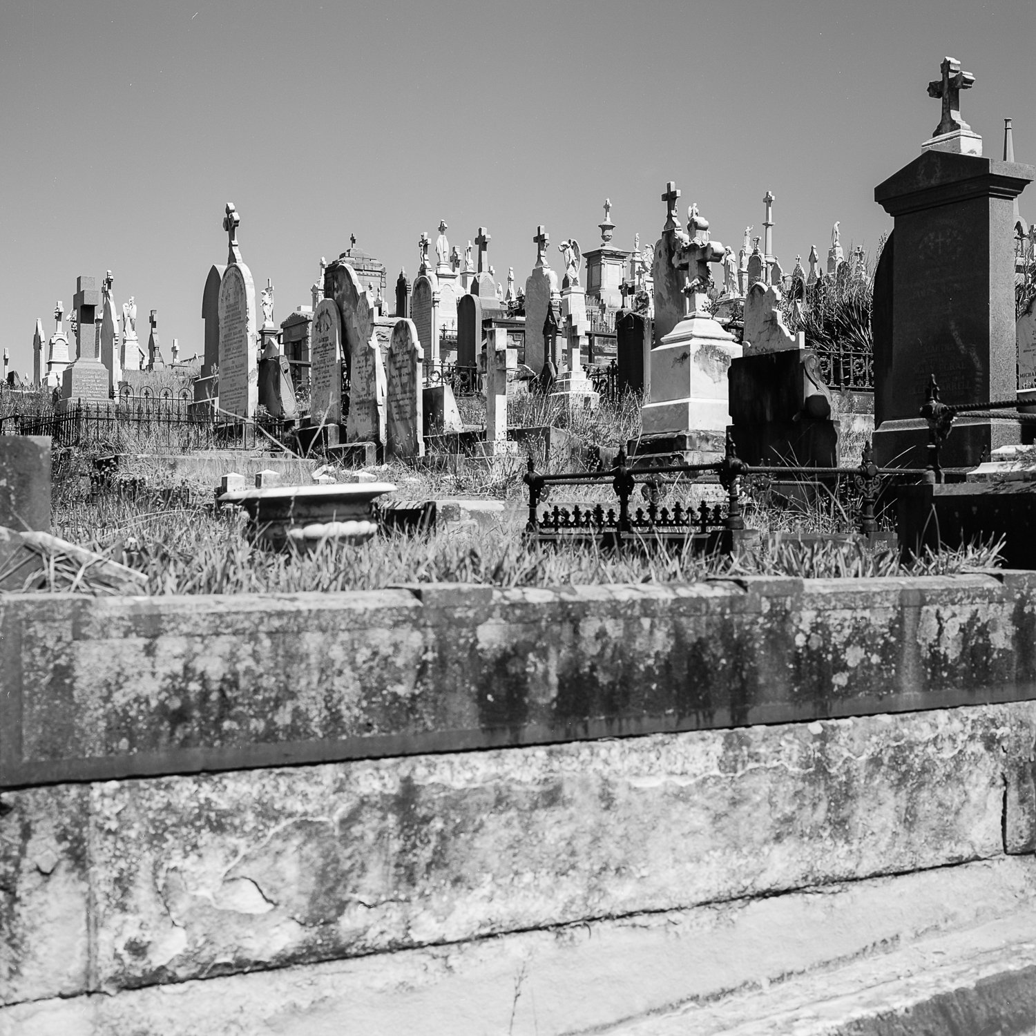 Black and white photo of a graveyard with numerous tombstones and crosses on a hillside.