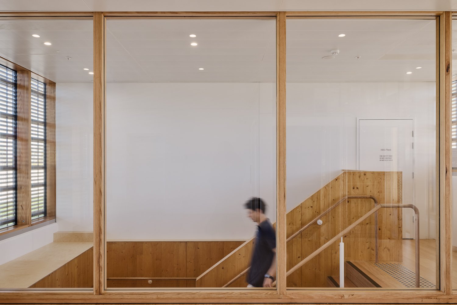 Interior view of a modern staircase with wooden accents, glass walls, and a blurred person walking down the stairs.