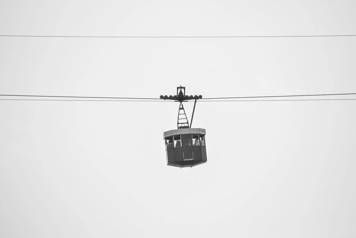 Black and white photo of a cable car hanging from wires in the sky with a minimalistic background.