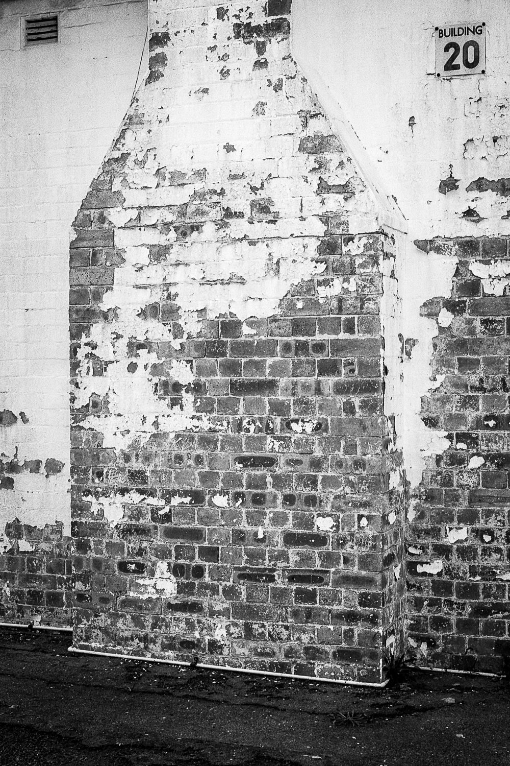 A brick wall with peeling paint and an attached chimney-like structure. There is a building number sign that reads 'BUILDING 20' in the upper right corner.