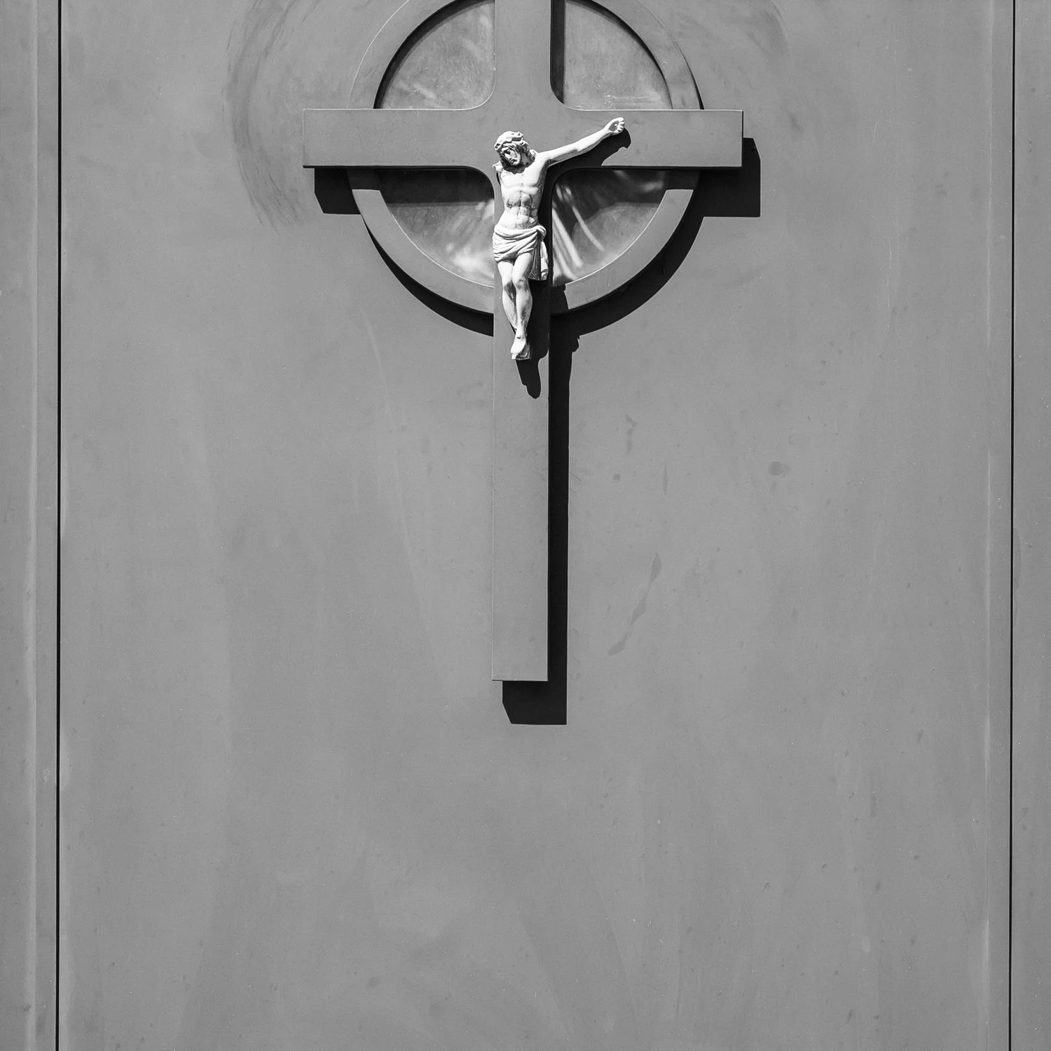 Black and white photo of a crucifix with Jesus Christ mounted on a wall.
