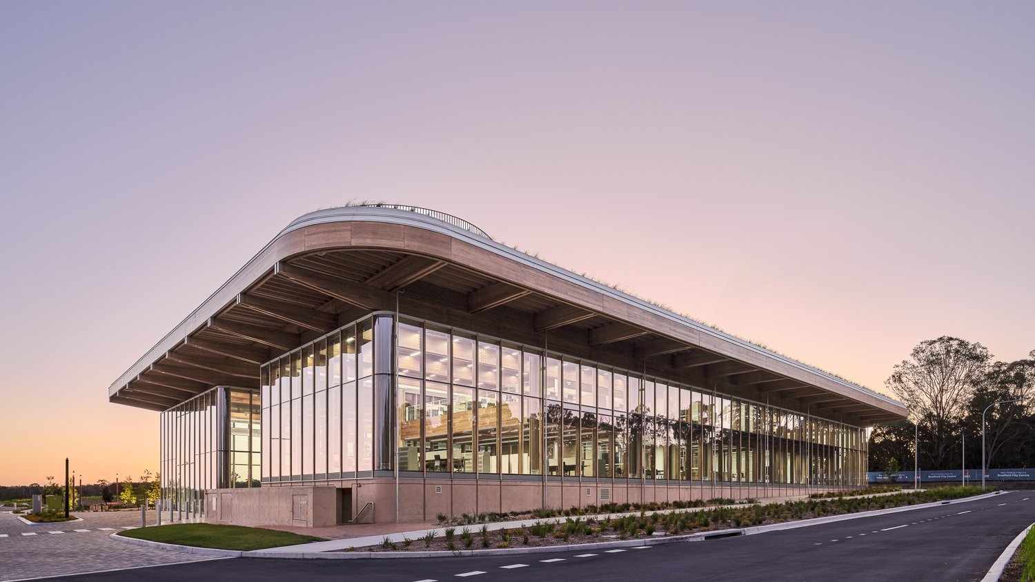 Modern building with extensive glass windows and curved roof at sunset.